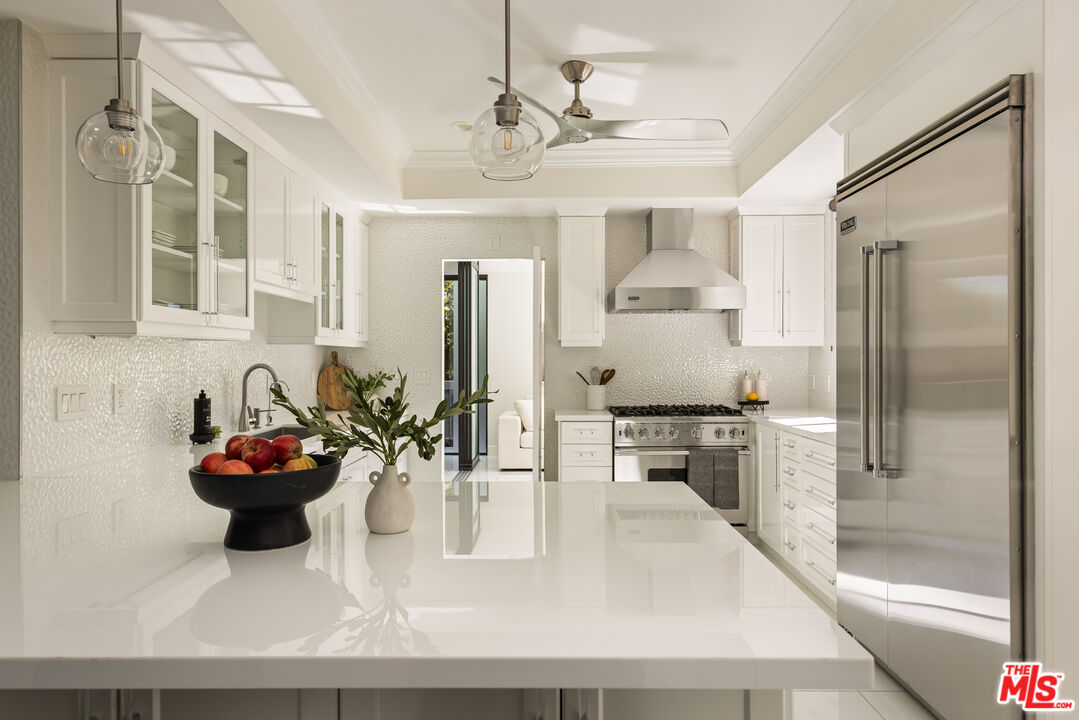 Bright white kitchen with a glossy island, stainless-steel appliances, and pendant lights.