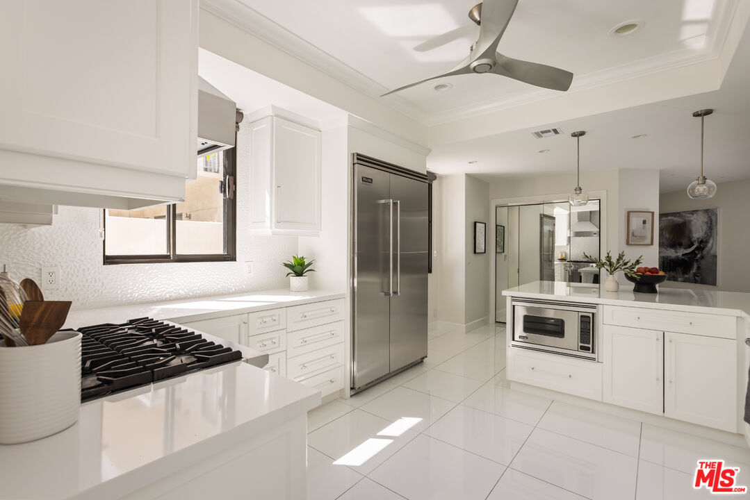 White kitchen with stainless steel refrigerator, gas cooktop, and island with built-in microwave