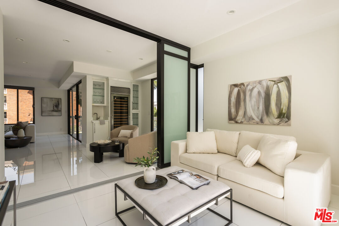 Staged living room with a cream sofa, tiled floors, and a bar area with a wine refrigerator.