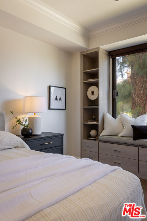 Bedroom with a white bed, built-in window seat and storage, and a large window overlooking trees.