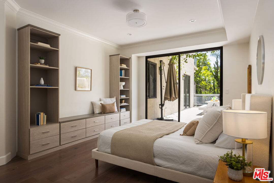 Staged bedroom with a white upholstered bed and built-in shelving beside glass doors to a sunny patio.