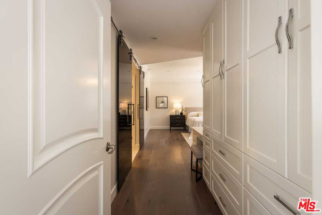 Bedroom beyond a dressing passage lined with white built-in wardrobes and dark wood flooring.