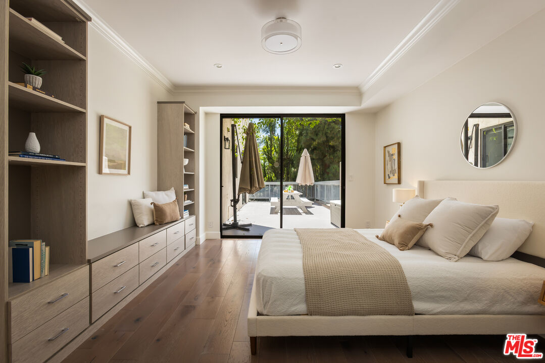 Staged bedroom with built-in wood shelving and sliding doors opening to a tree-lined patio.