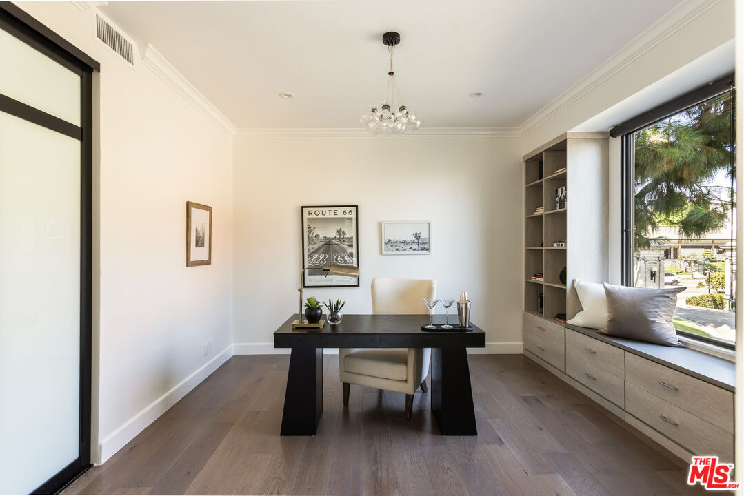 Staged home office with a black desk, cream chair, built-in window seat, and large street-facing window.