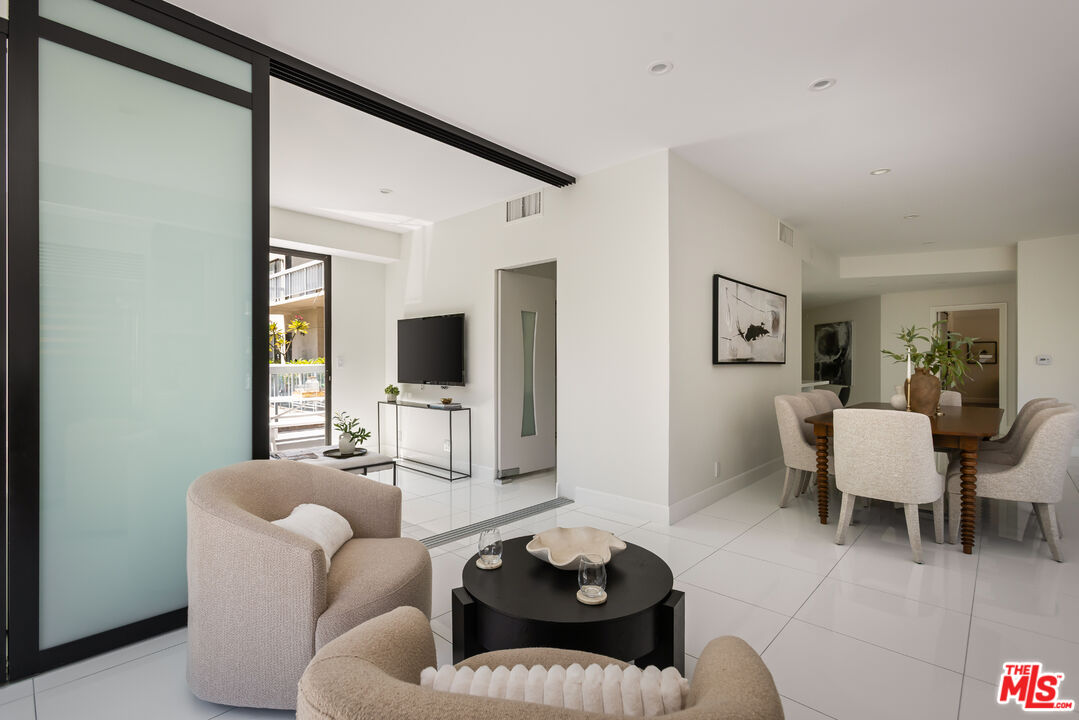 Open-plan living and dining room with white tile floors, upholstered chairs, and a frosted-glass sliding panel.
