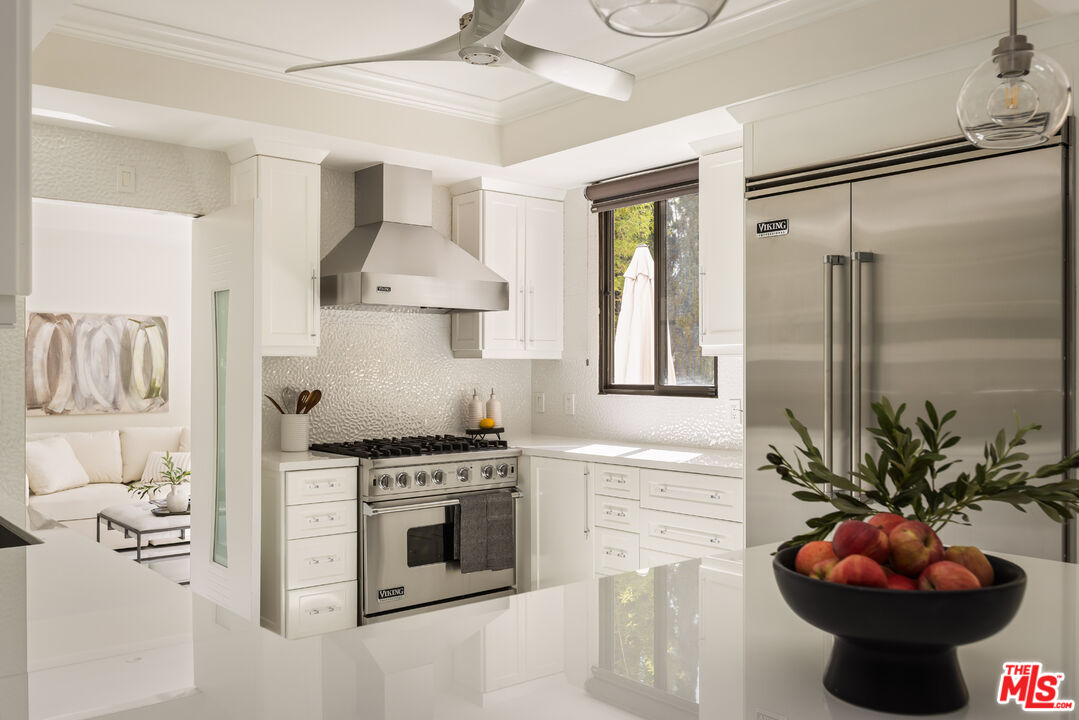 White kitchen with stainless-steel Viking appliances, glossy counters, and a fruit bowl on the island.