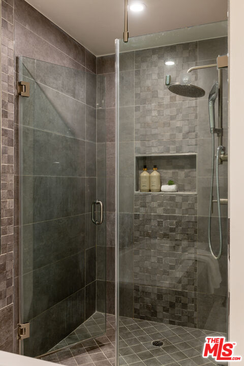 Walk-in shower with gray tile, a glass enclosure, rainfall showerhead, and recessed niche.