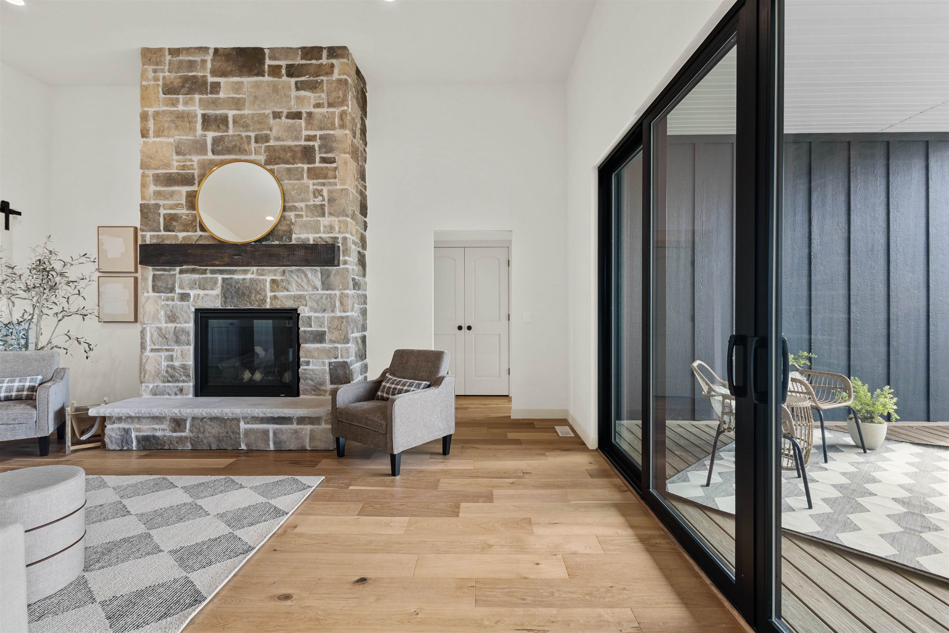 Living room with a tall stone fireplace, gray seating, and sliding glass doors to a covered patio.