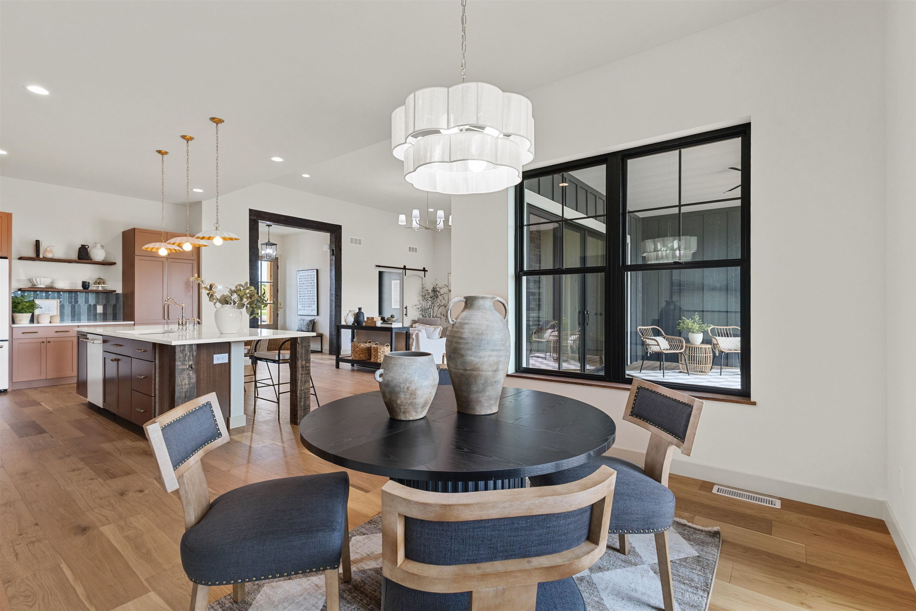 Dining area with a round black table and chandelier beside large windows overlooking a covered patio.