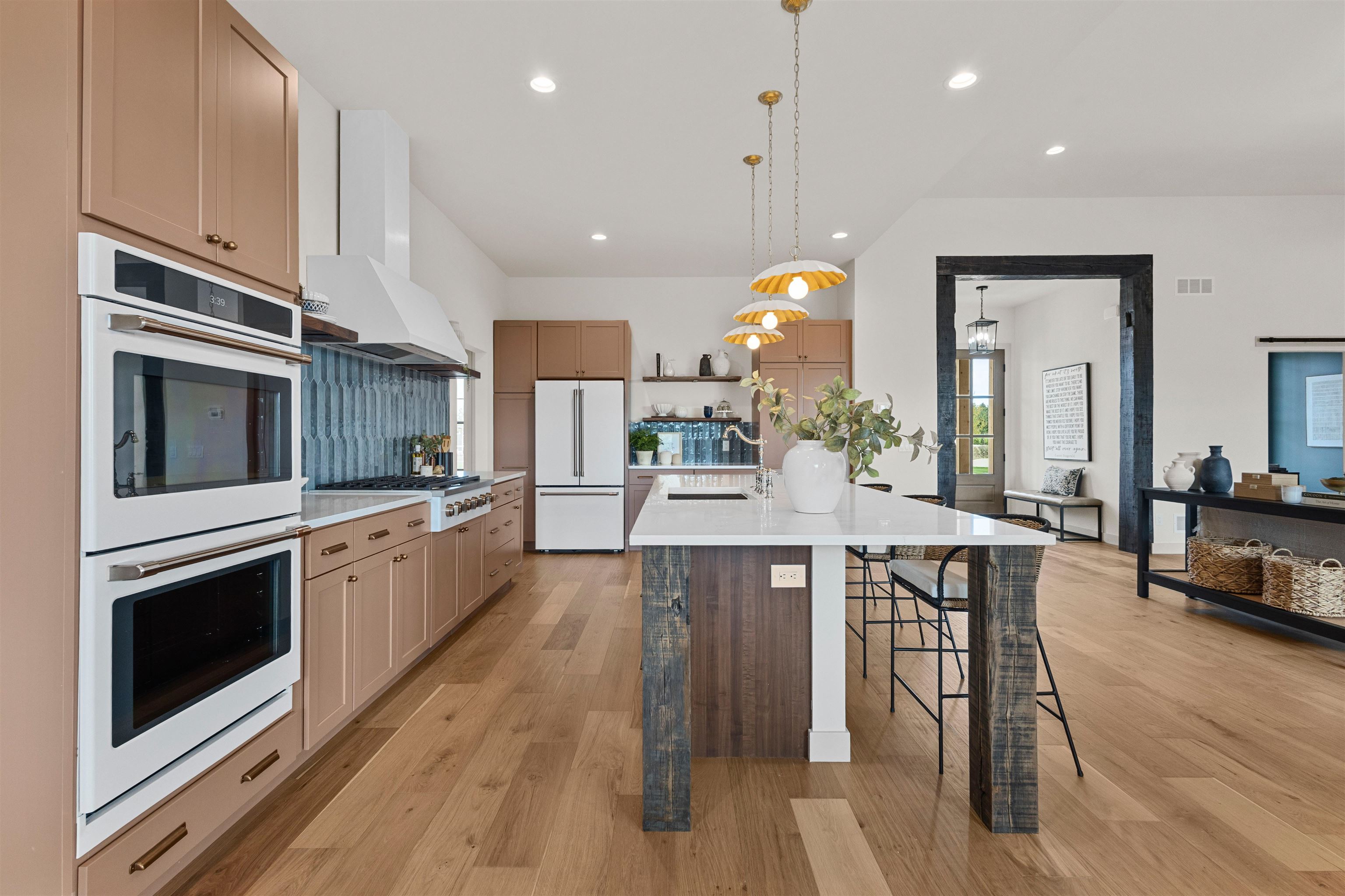 Kitchen with taupe cabinets, blue tile backsplash, double ovens, and a large island with bar seating.