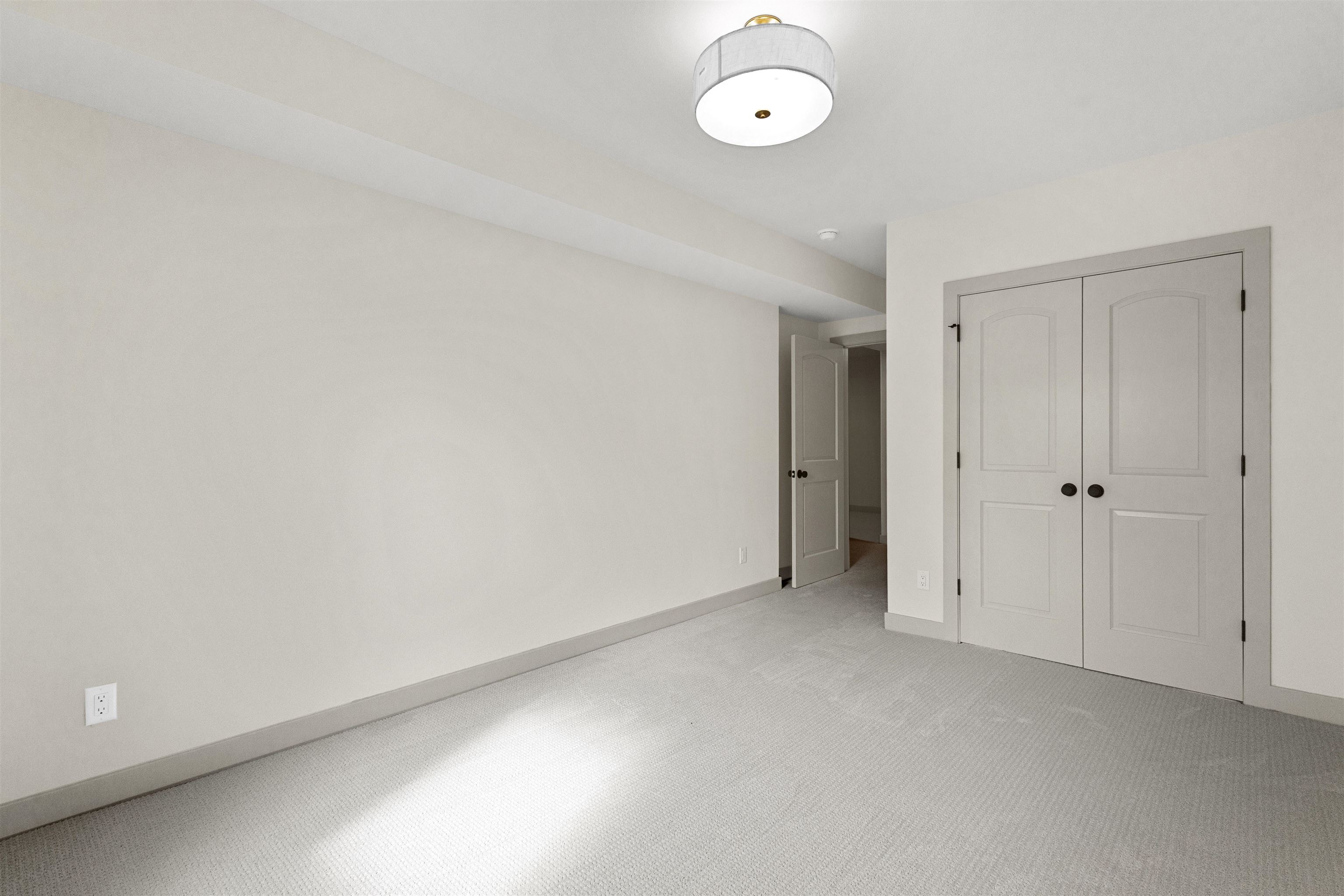 Empty carpeted room with double closet doors and an open doorway to the hall.