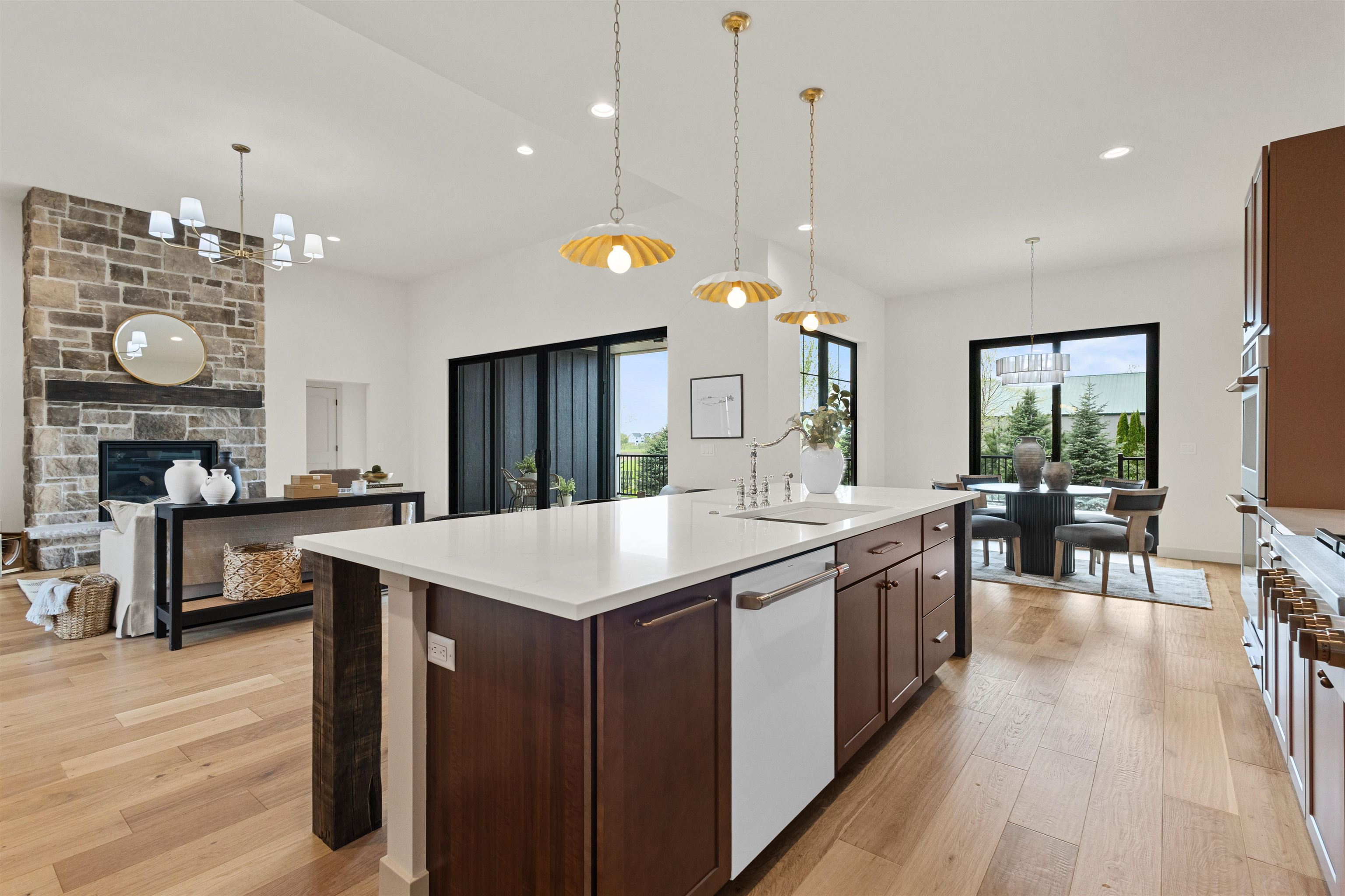 Open-plan kitchen with a large white island, dark cabinetry, stone fireplace, and light wood floors.