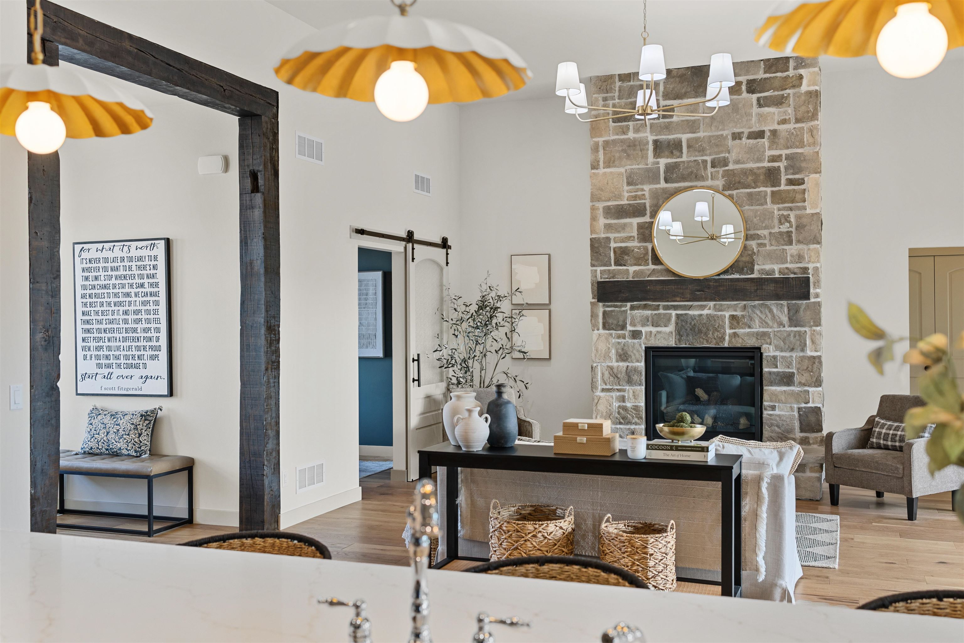Staged living room with a tall stone fireplace, dark wood mantel, and barn-style doorway.