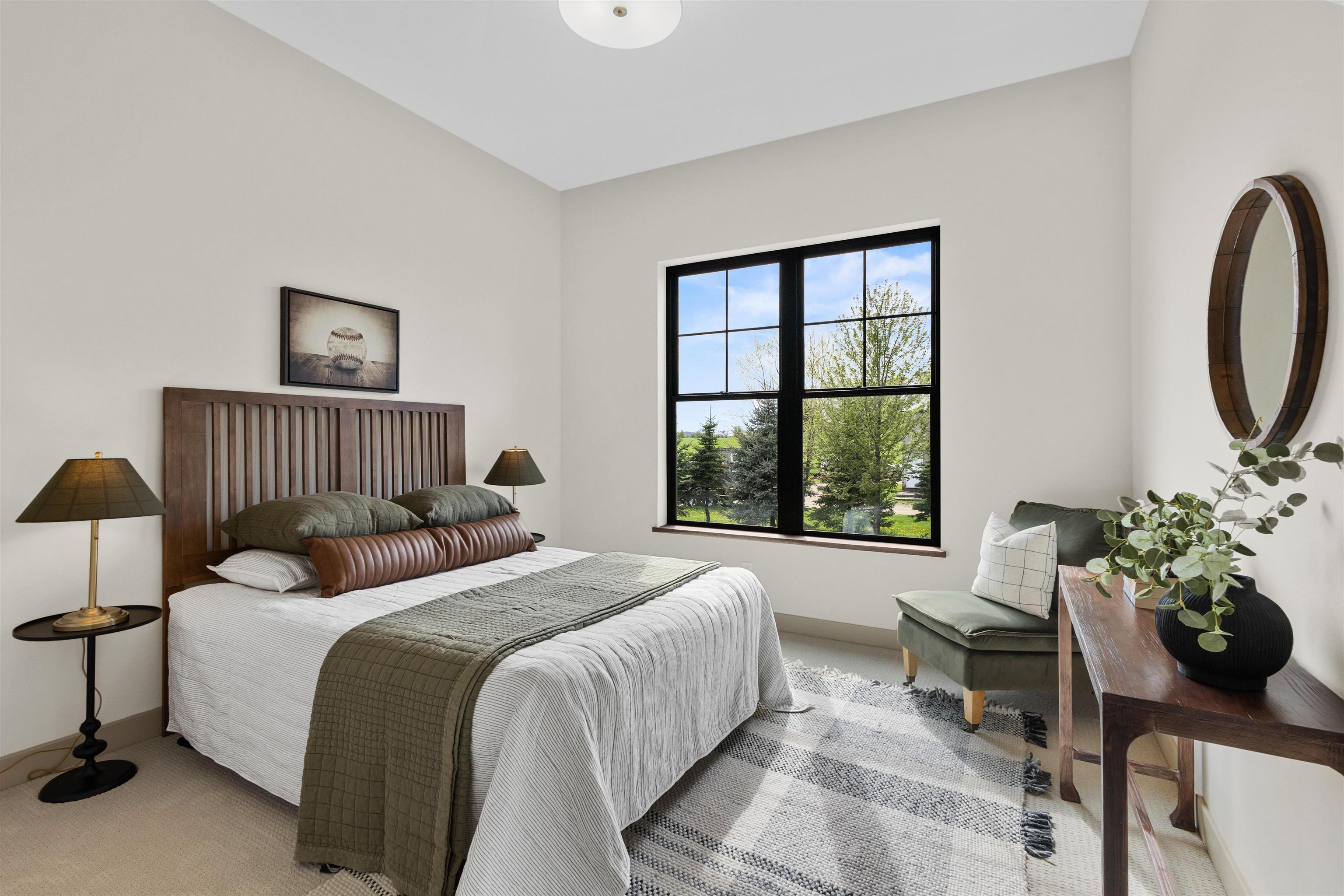 Staged bedroom with a wooden slatted headboard, black-framed window, green chair, and patterned rug.