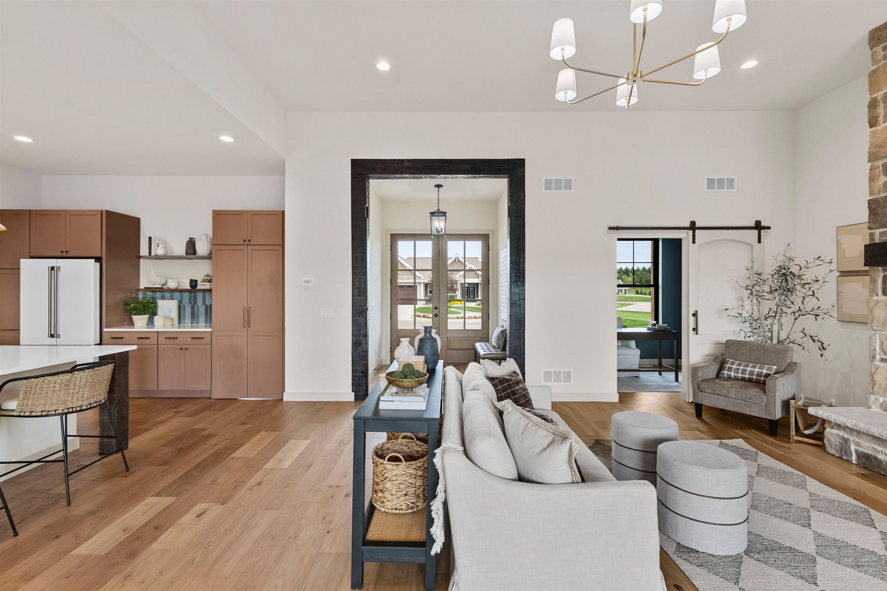 Open-plan living room and kitchen with brown cabinets, warm wood floors, and a furnished sitting area.