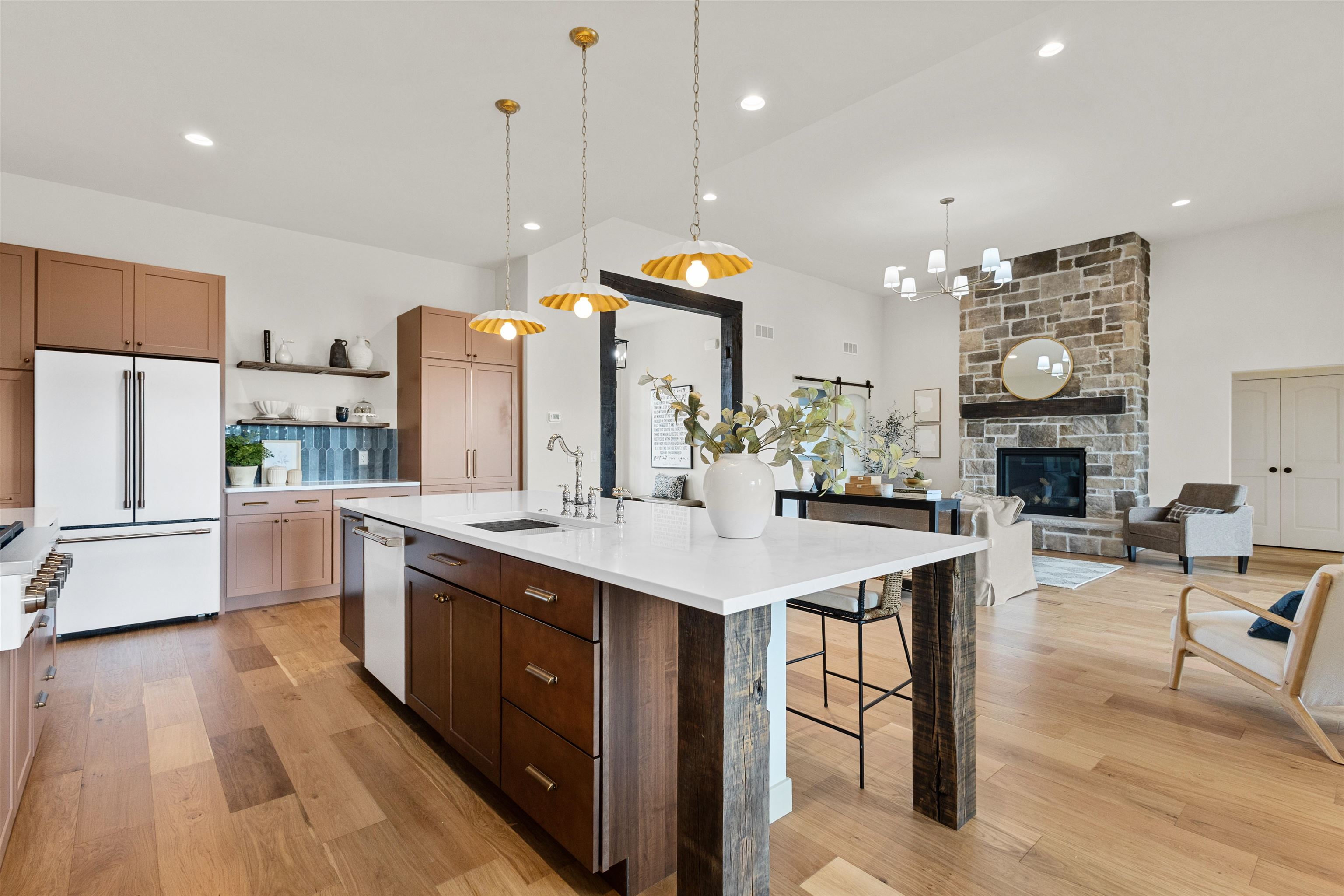 Open kitchen with a large white island and muted rose cabinets beside a stone fireplace.