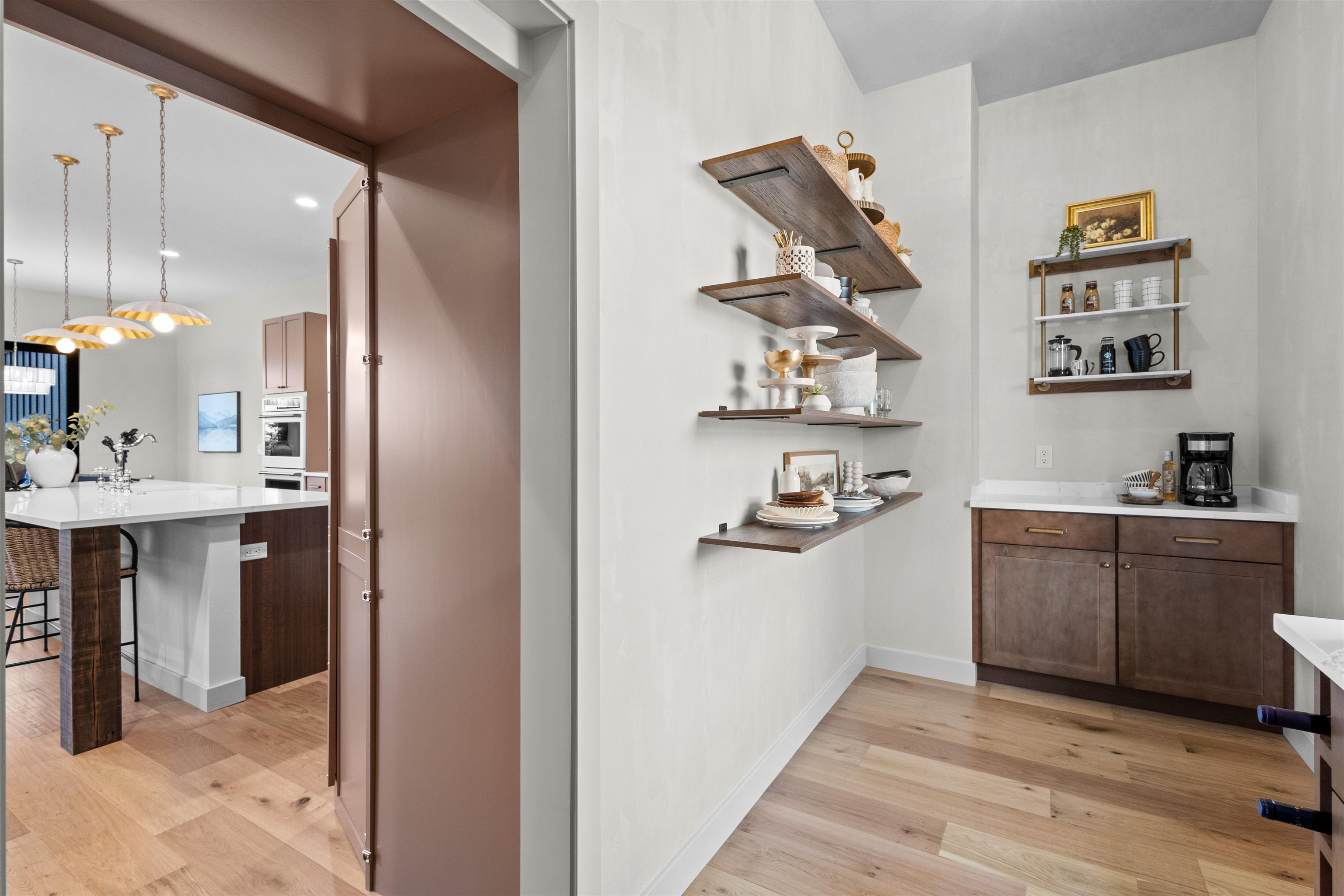 Kitchen coffee station with floating shelves, dark wood cabinetry, and a white countertop.