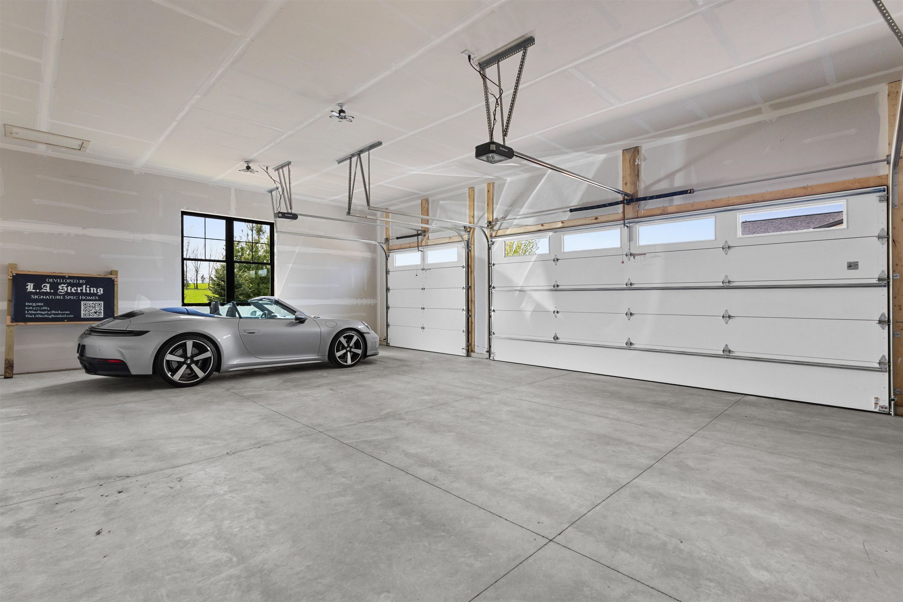 Spacious garage with two large doors, a gray convertible, and a black-framed window.