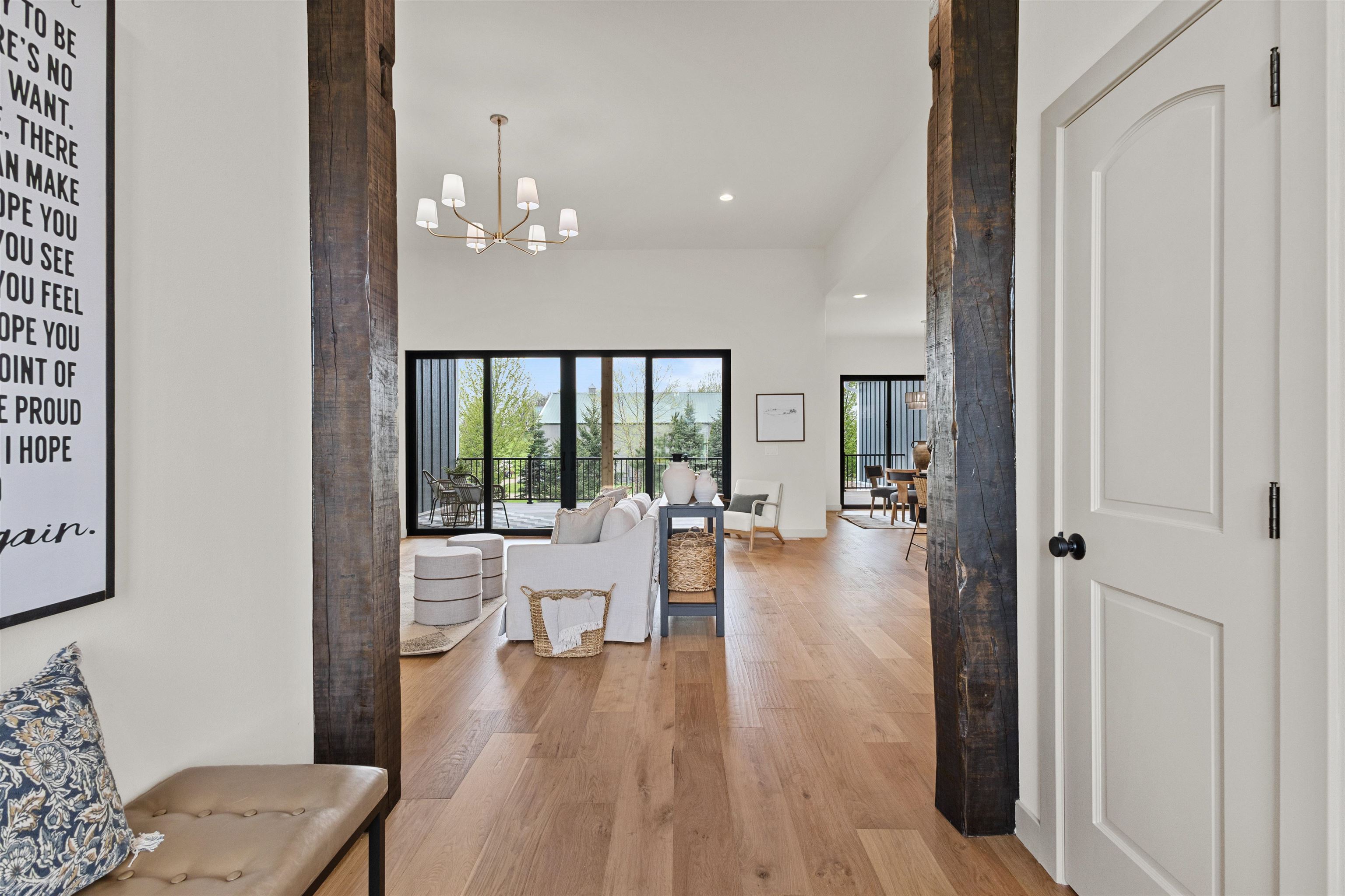 Open-plan living room with dark timber doorway posts, a white sofa, wood floors, and balcony doors.