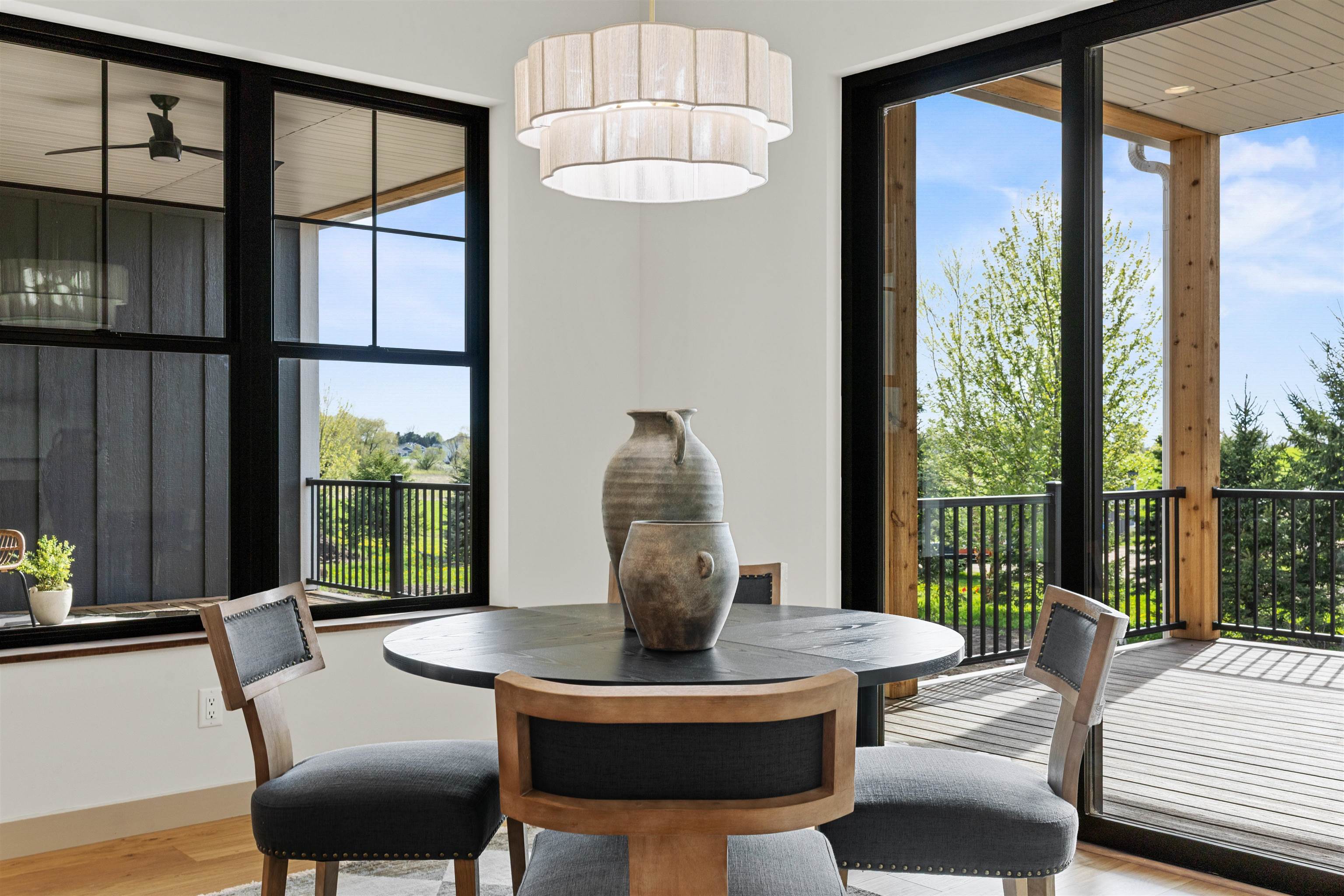 Dining room with a round table and chandelier beside large windows opening onto a covered deck.