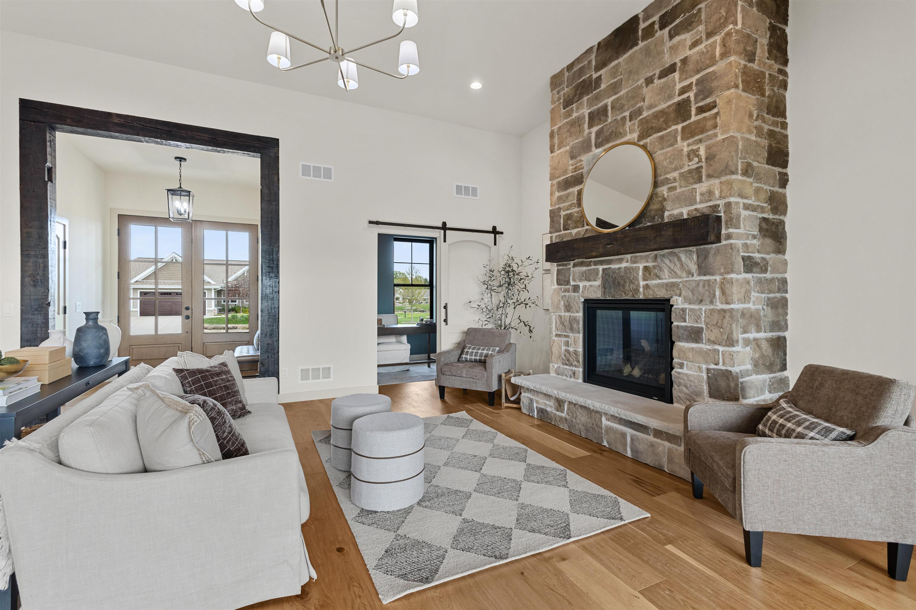 Staged living room with a floor-to-ceiling stone fireplace, pale seating, and French doors.
