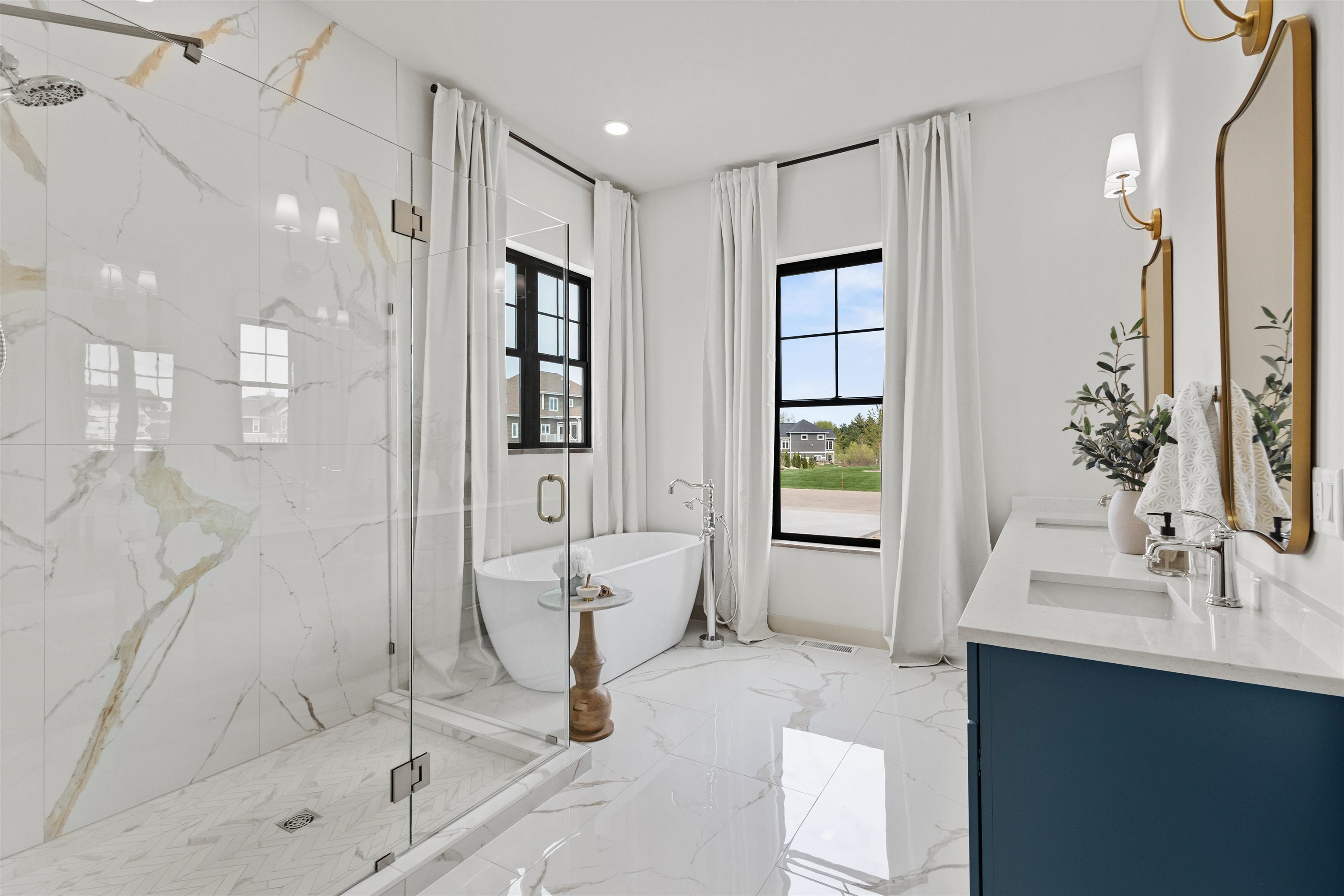 Bright primary bathroom with a veined tile shower, freestanding tub, and navy double vanity.