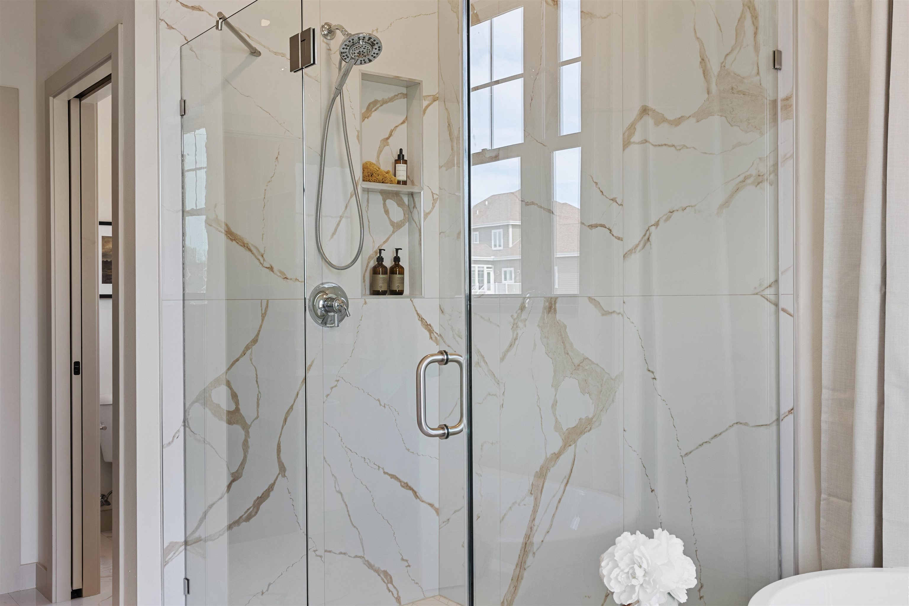 Glass-enclosed shower with chrome fixtures, marble-look walls, and built-in toiletry niches.