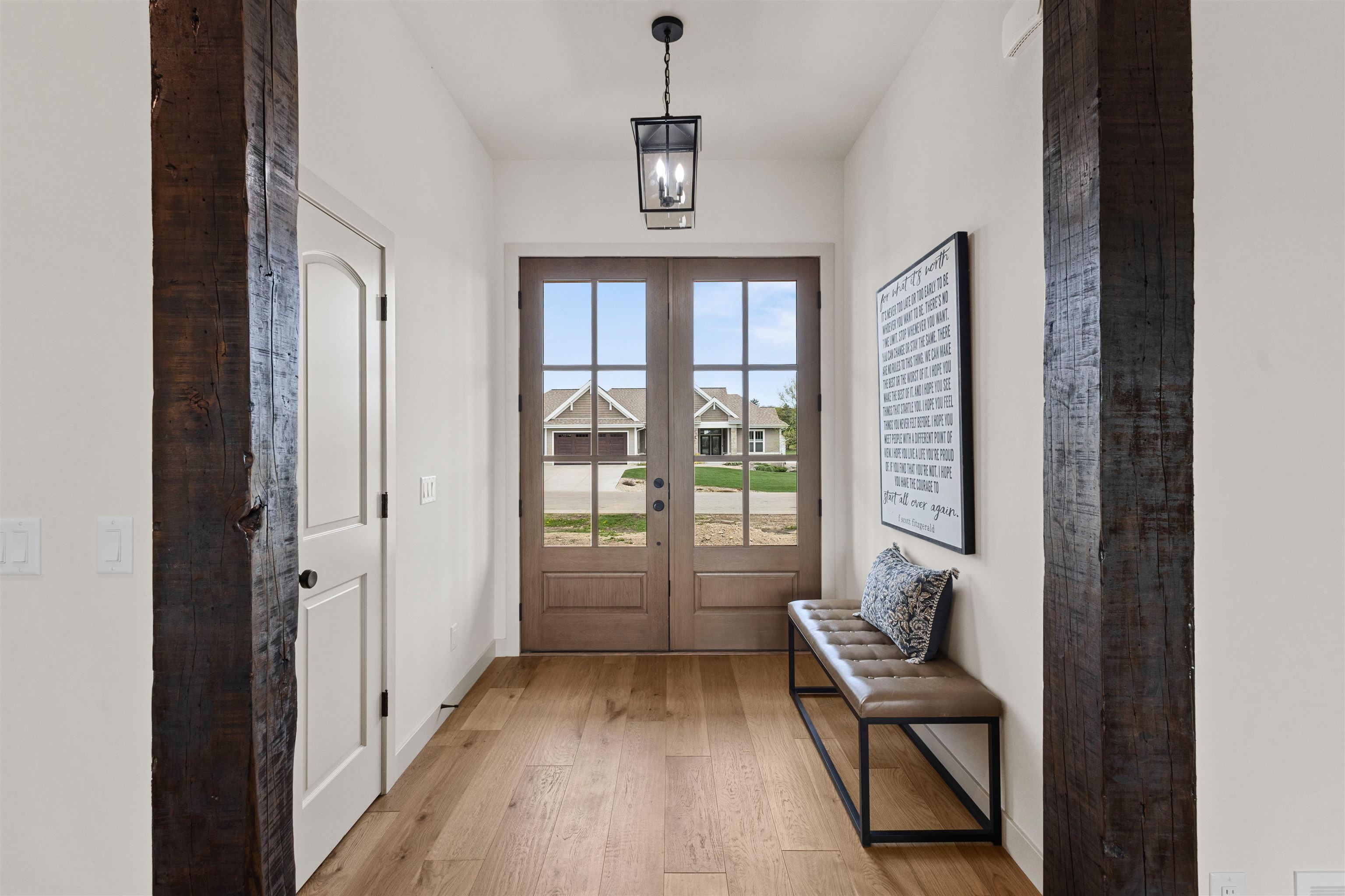 Entry foyer with rustic timber beams, glass-paneled double doors, and a bench along the wall.