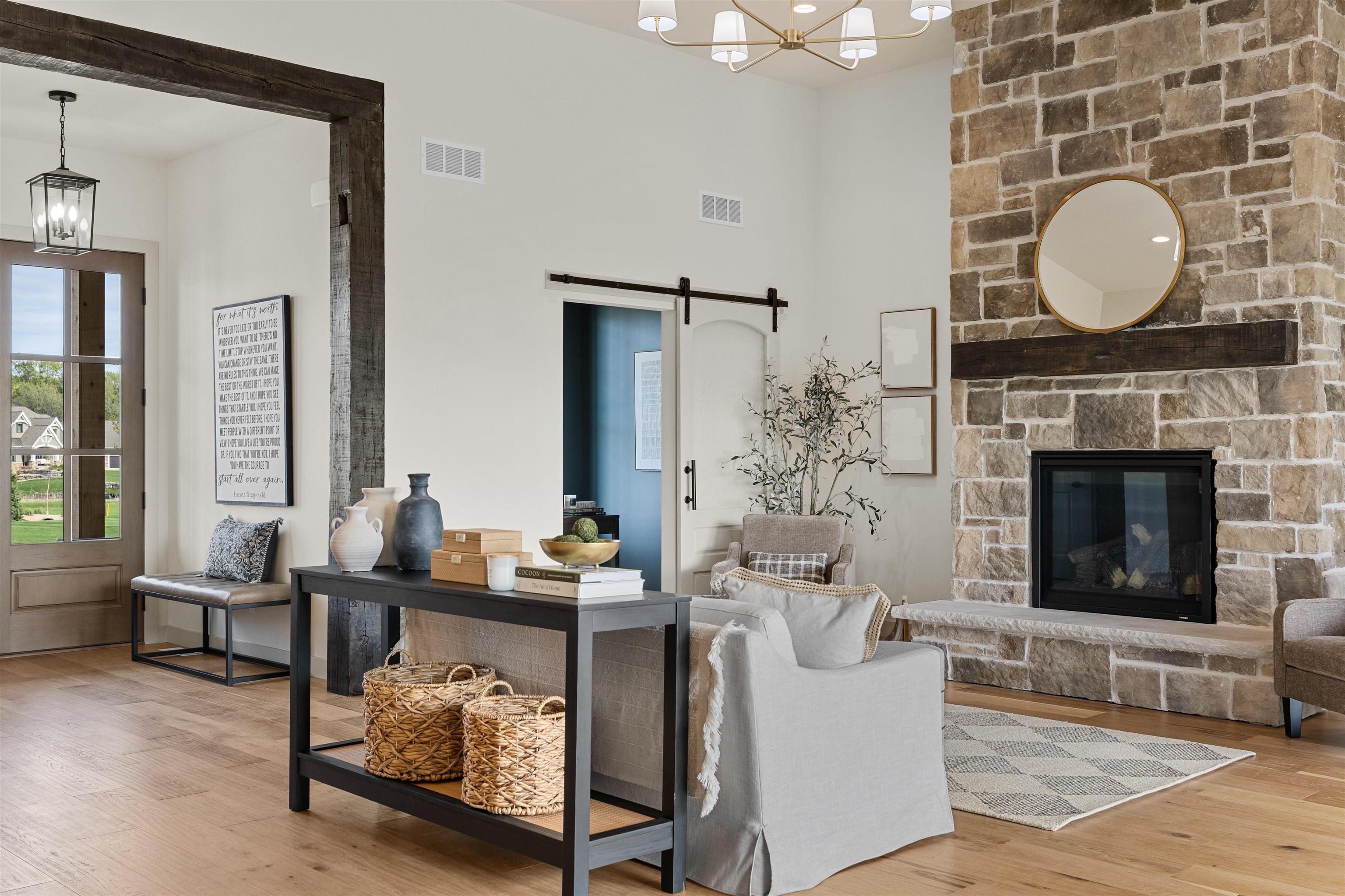 Staged living room with a tall stone fireplace, dark exposed beam, and sliding barn door.