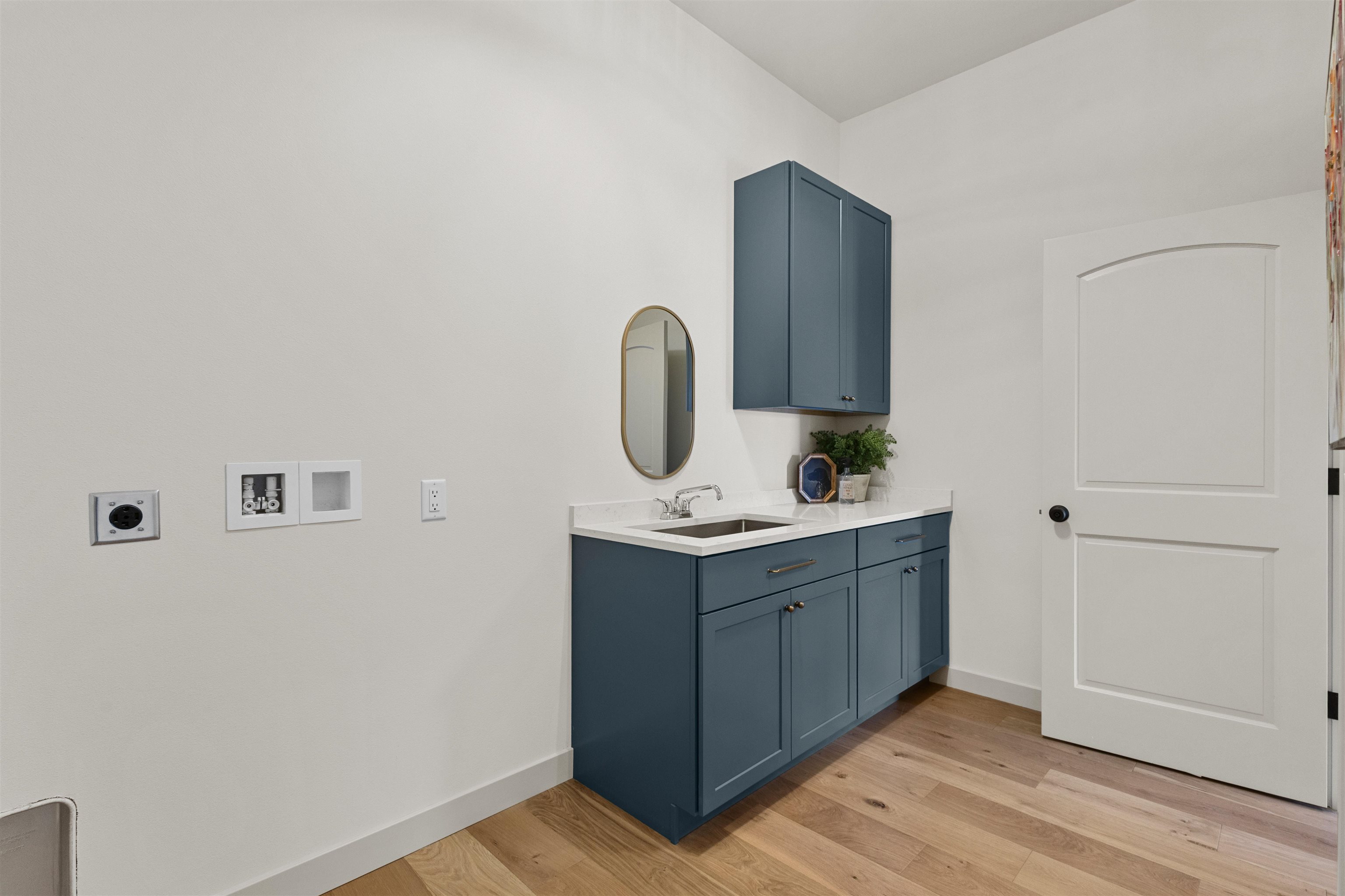 Bathroom with a deep blue vanity, oval mirror, white countertop, and warm wood flooring.