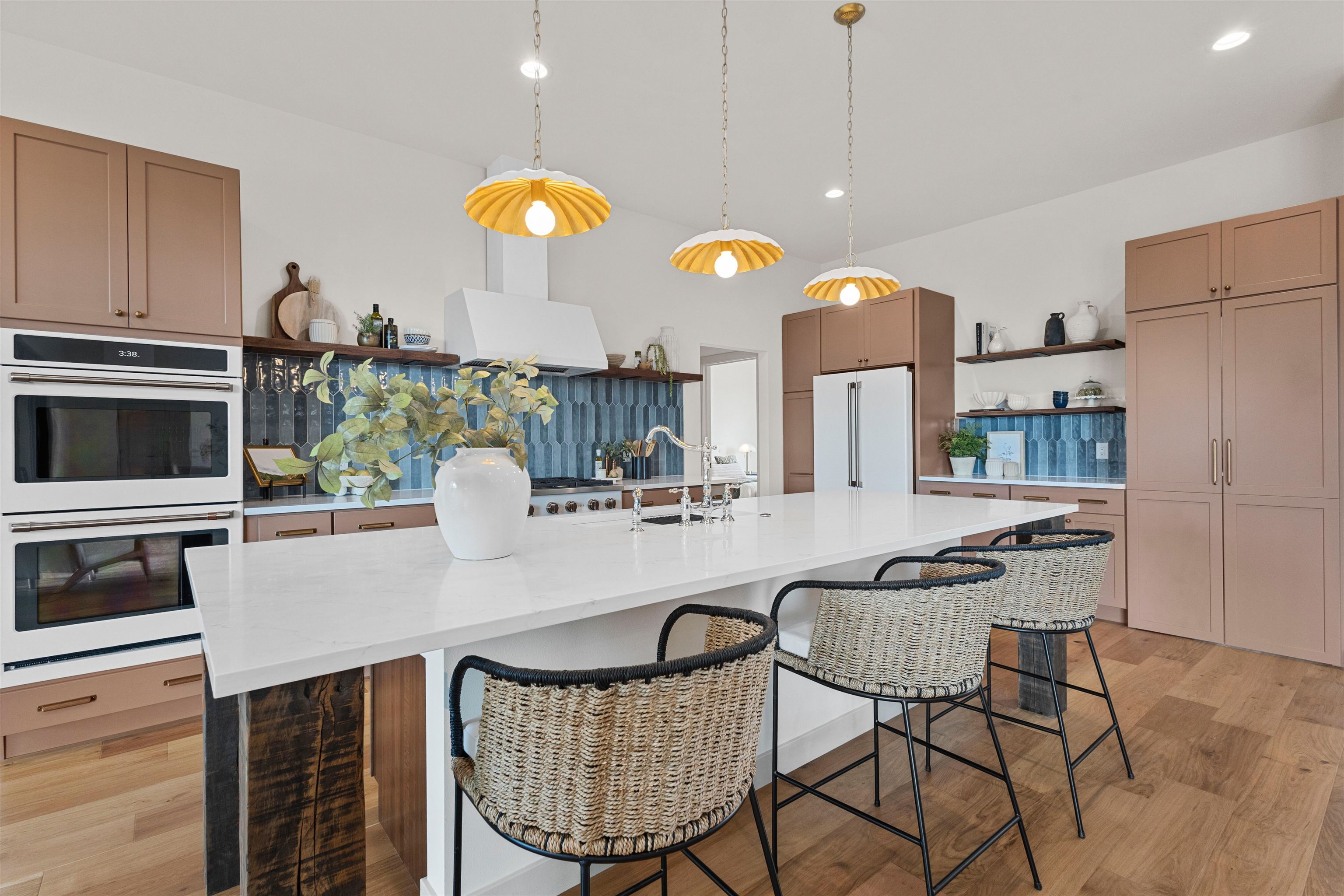 Modern kitchen with a large white island, blue tile backsplash, and three gold pendant lights.