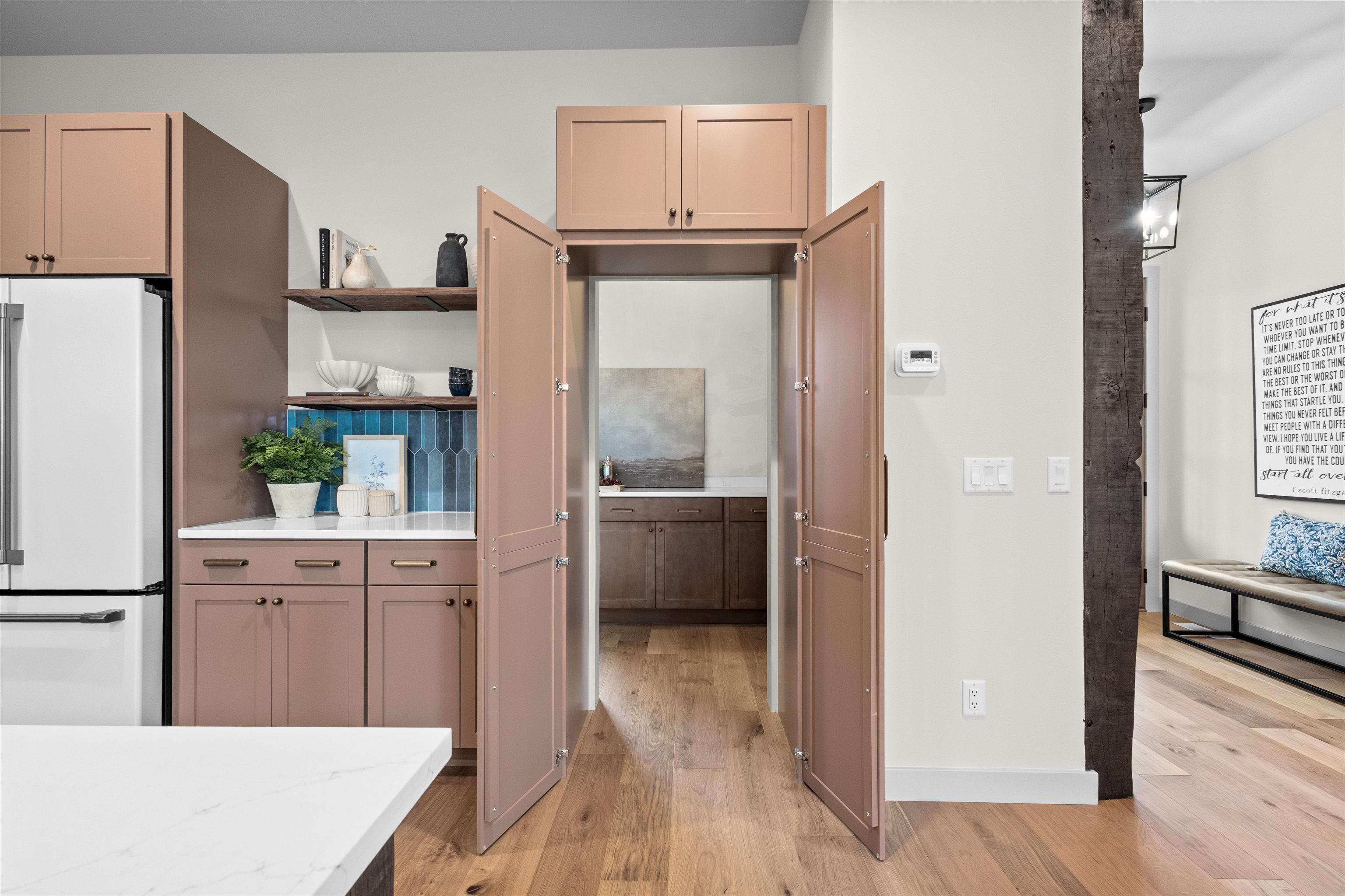 Kitchen with open pantry doors, dusty rose cabinets, blue tile backsplash, and a dark timber post.