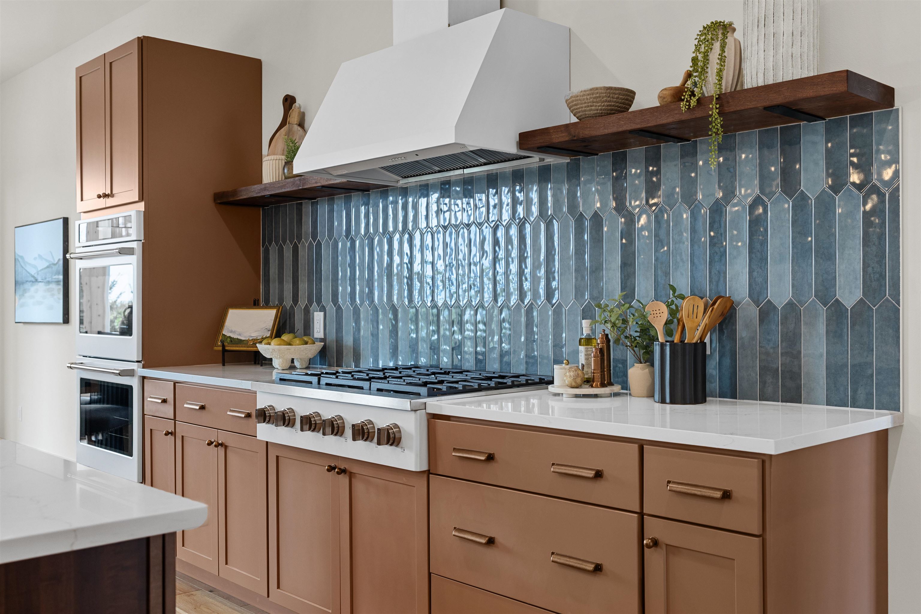 Modern kitchen with a wide gas range, blue tile backsplash, and warm brown cabinets.