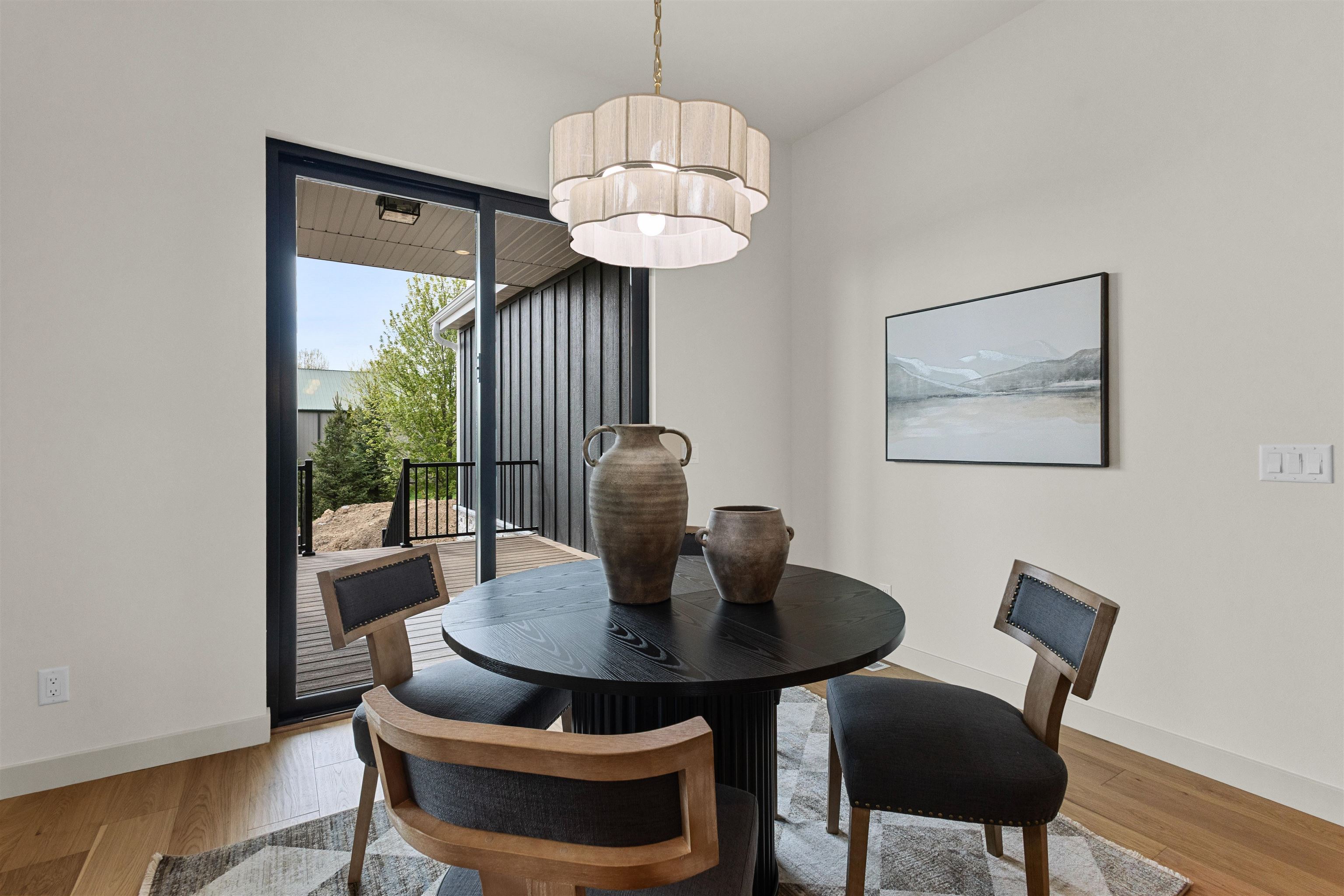 Dining room with a round black table and tiered chandelier beside sliding doors to a deck.