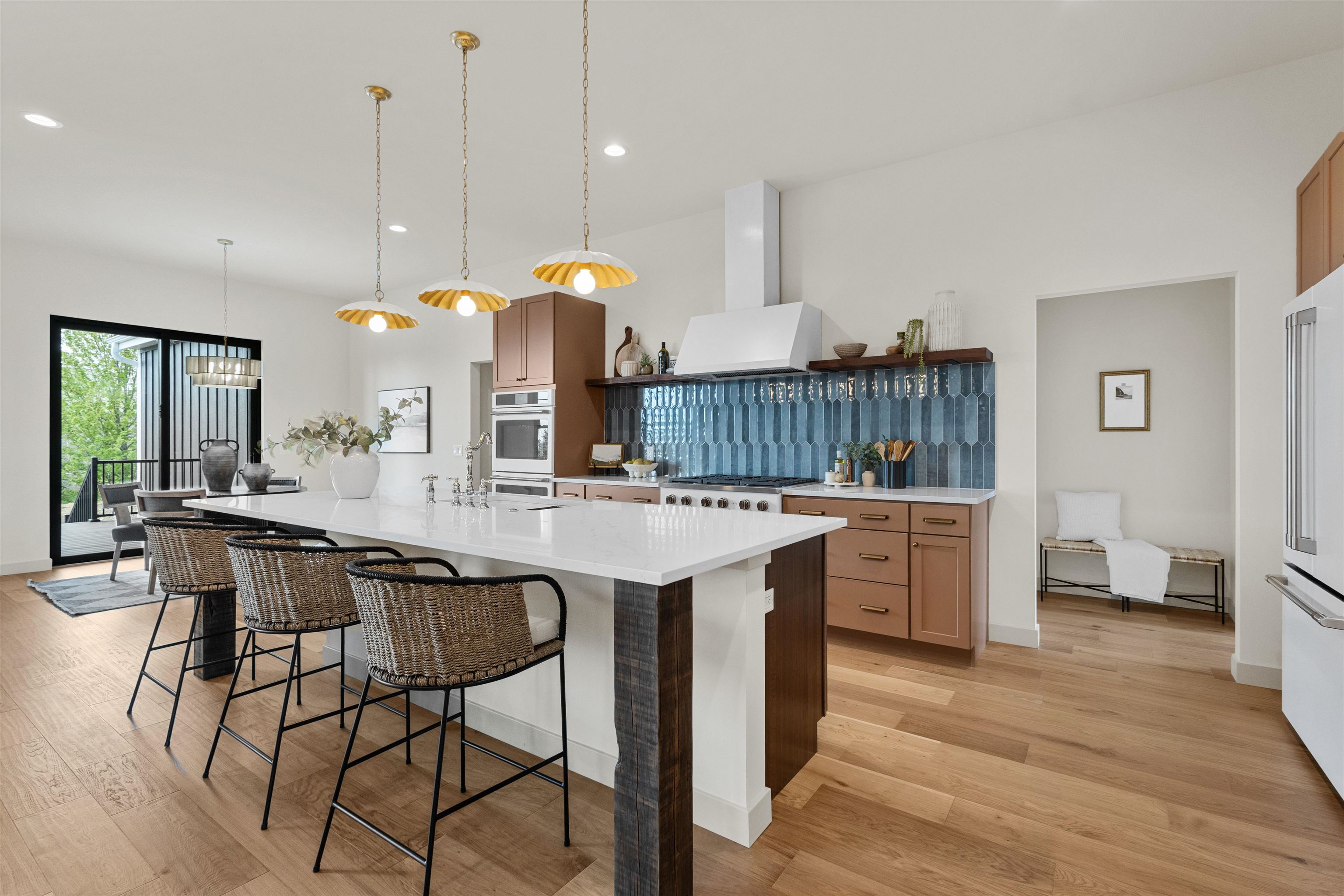 Modern kitchen with a white island, woven bar stools, blue tile backsplash, and warm wood cabinetry.