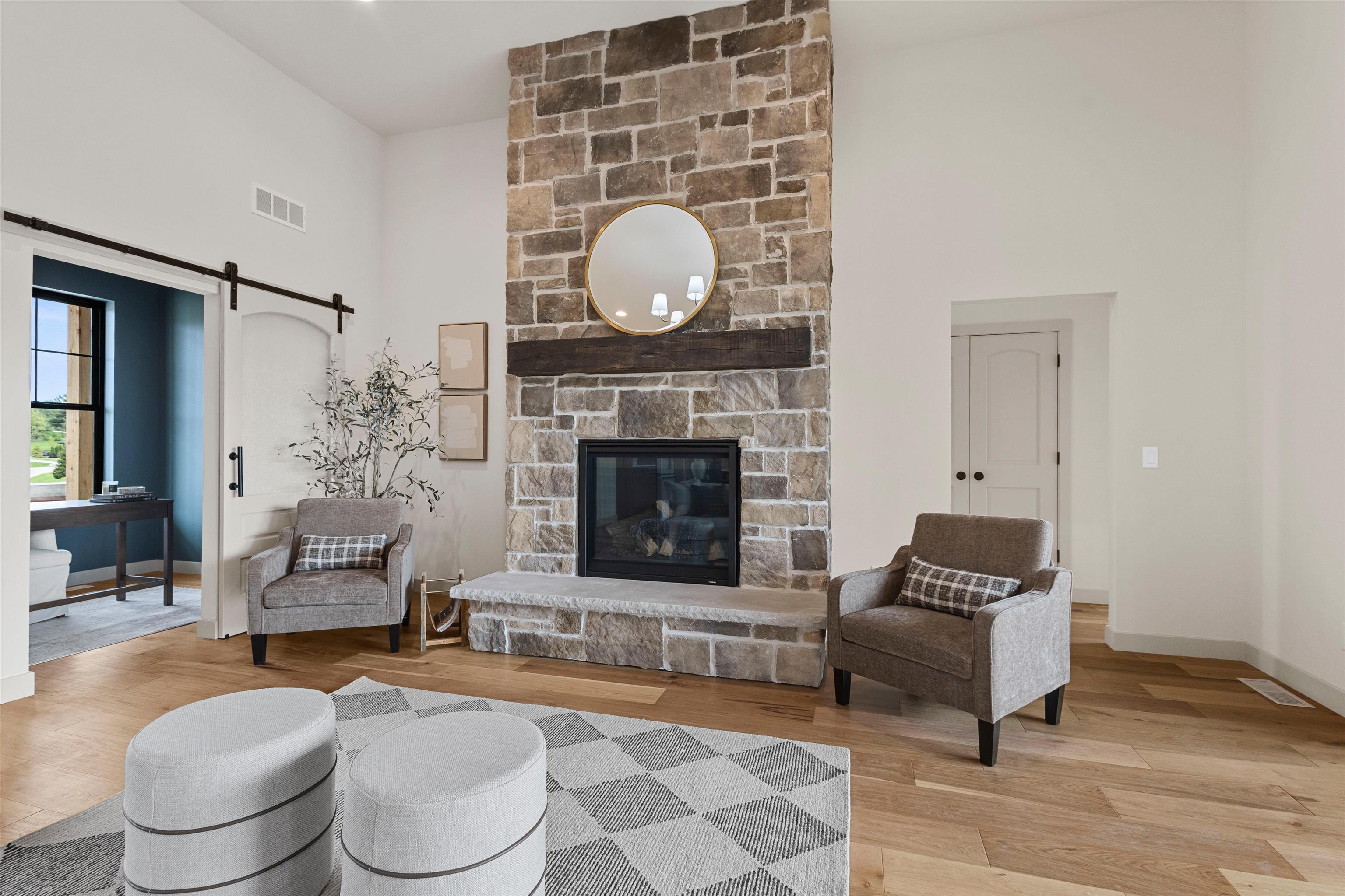 Living room with a floor-to-ceiling stone fireplace, round mirror, and two upholstered armchairs.