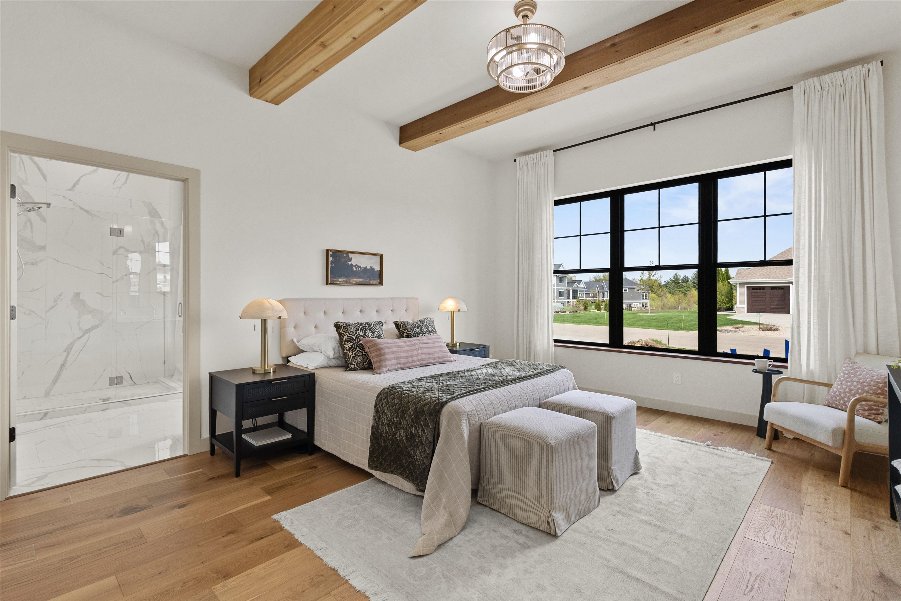Bedroom with exposed wood ceiling beams, a marble-tiled shower, and a large black-framed window.