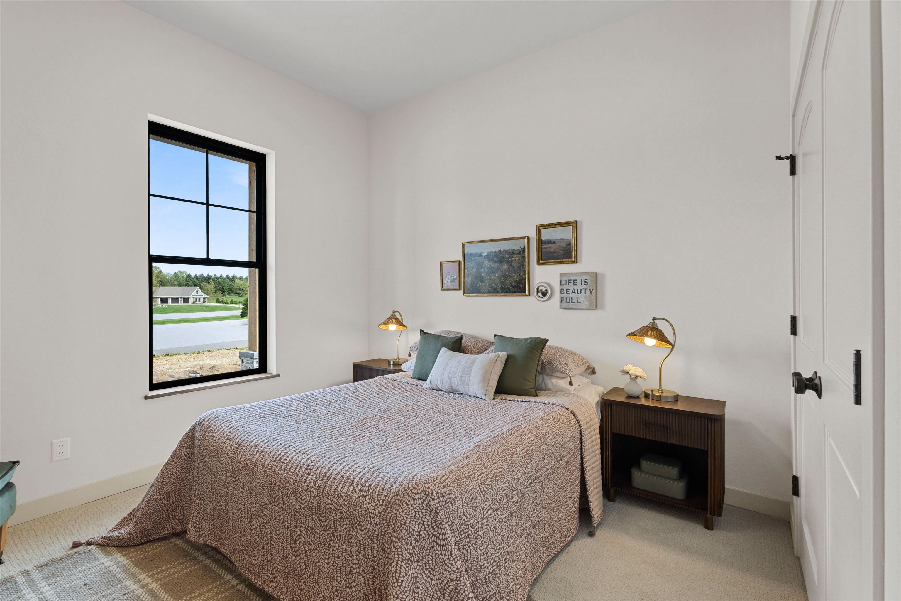 Bedroom with a patterned bedspread, brass bedside lamps, and a large black-framed window.