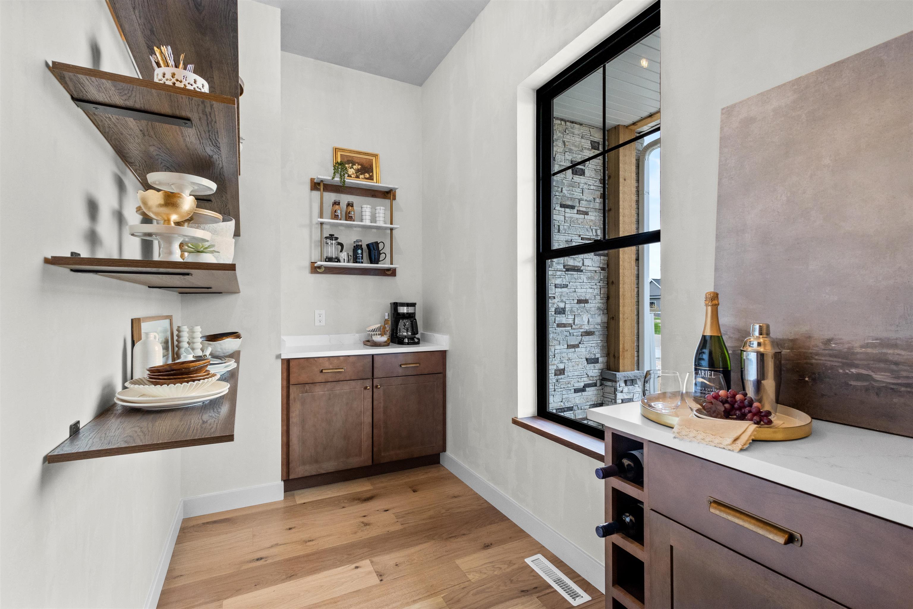 Beverage bar with dark wood cabinets, open display shelves, and a large black-framed window.