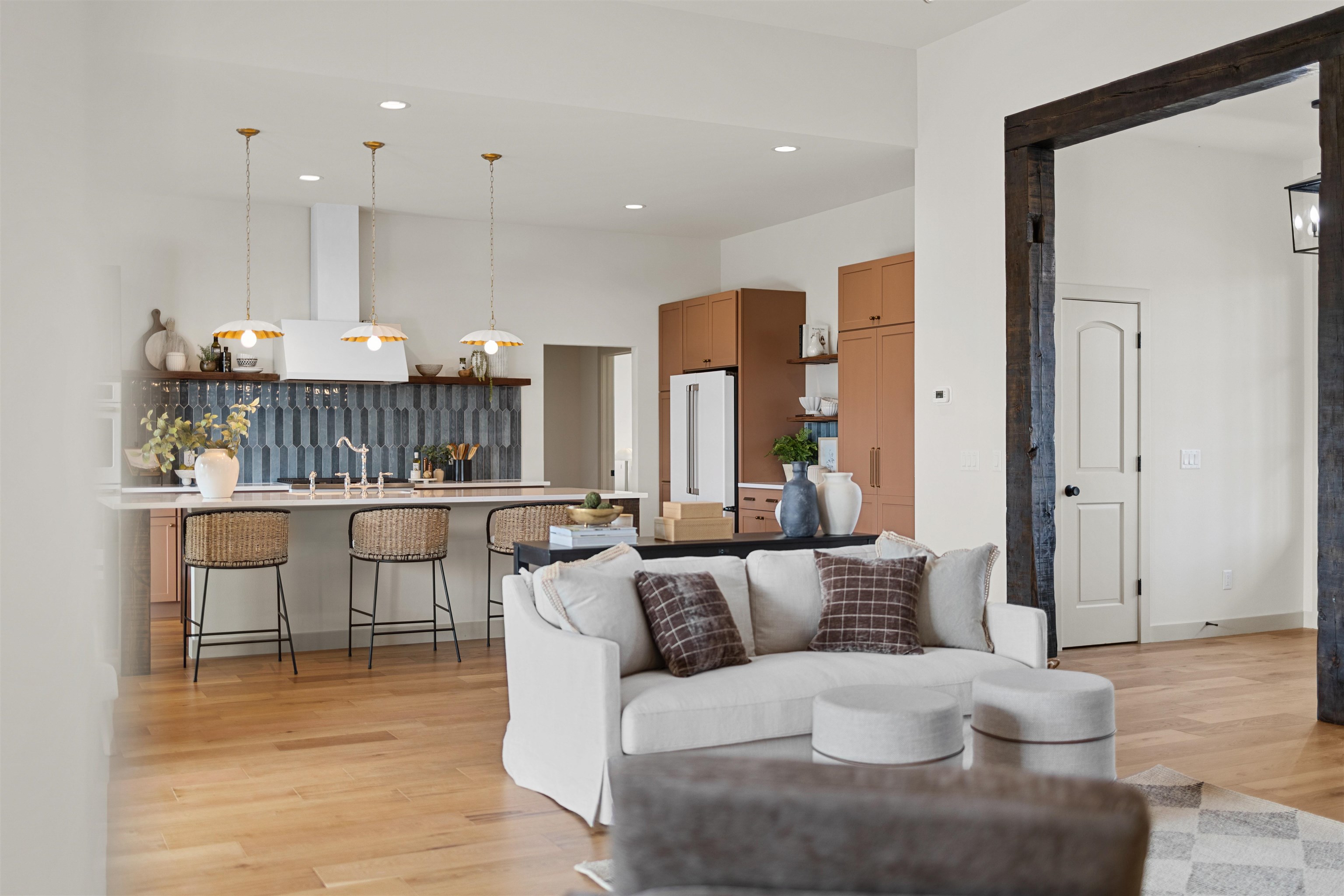 Open-plan kitchen and living room with a white sofa, blue-gray tile backsplash, and warm brown cabinetry.