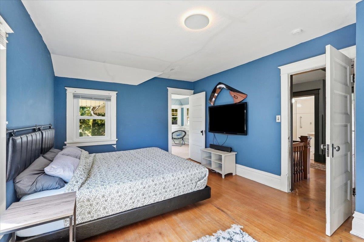 Bedroom with blue walls, a patterned bedspread, hardwood floors, and a wall-mounted television.