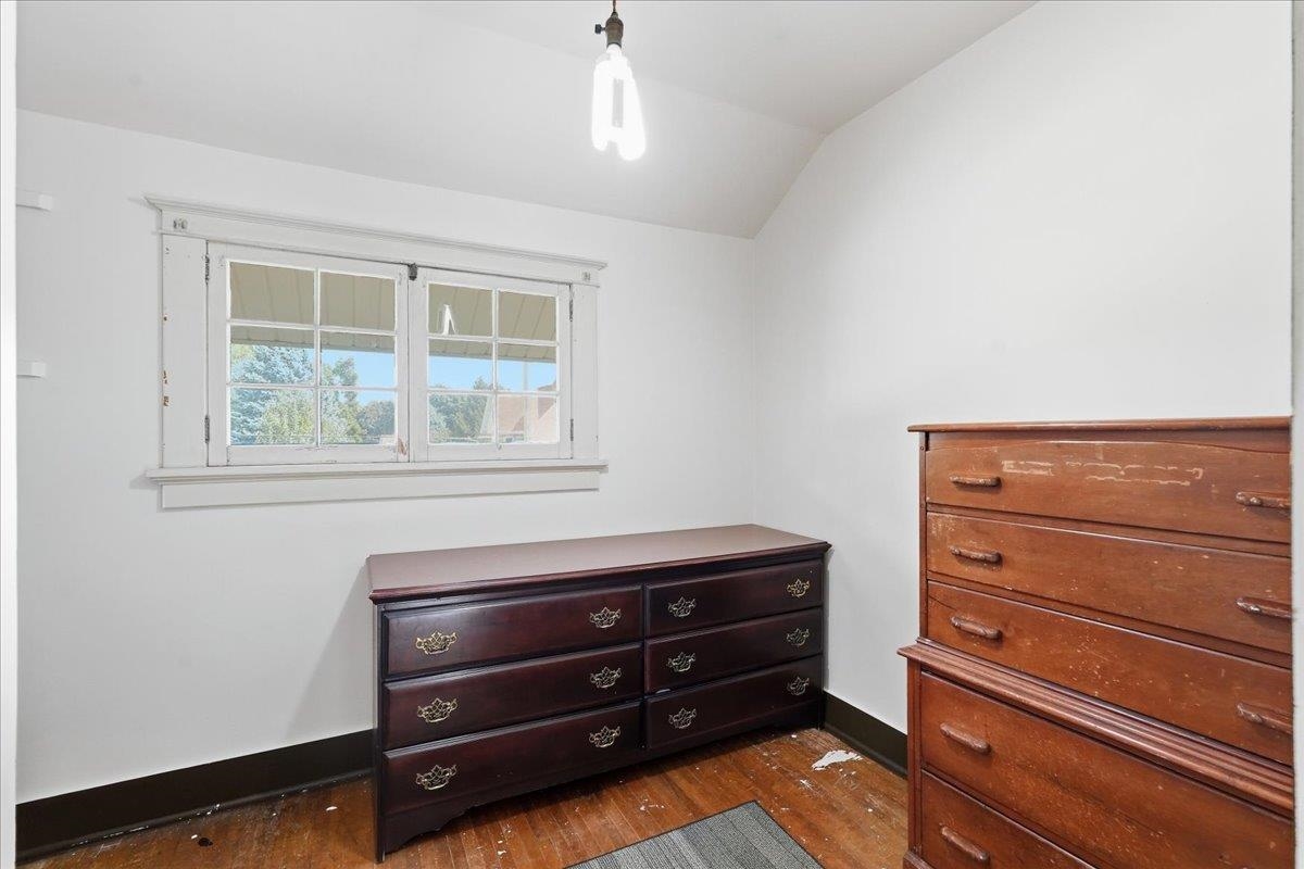 Bedroom with two wooden dressers, a multi-pane window, and worn hardwood floors.