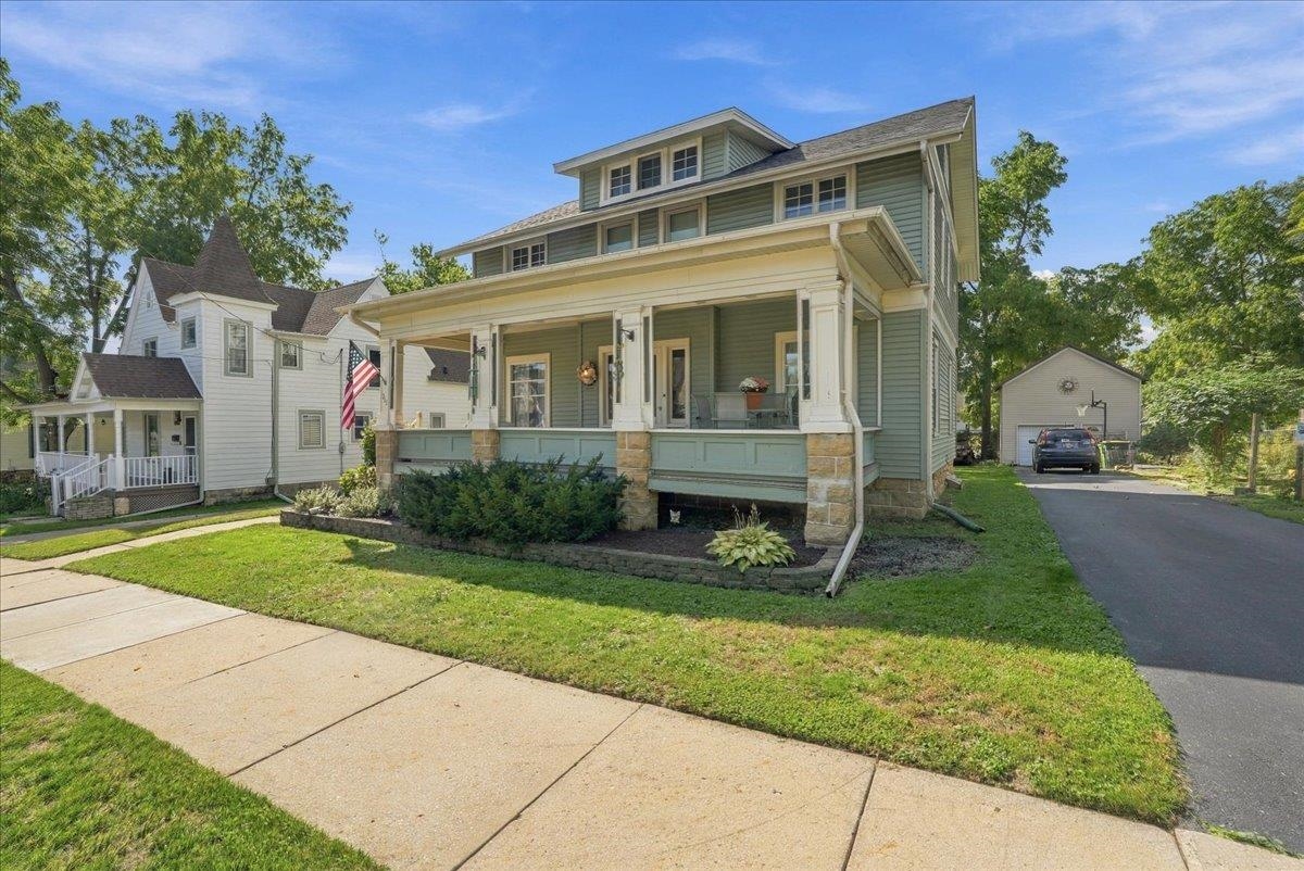 Green-sided house with a broad covered porch and driveway to a detached garage.