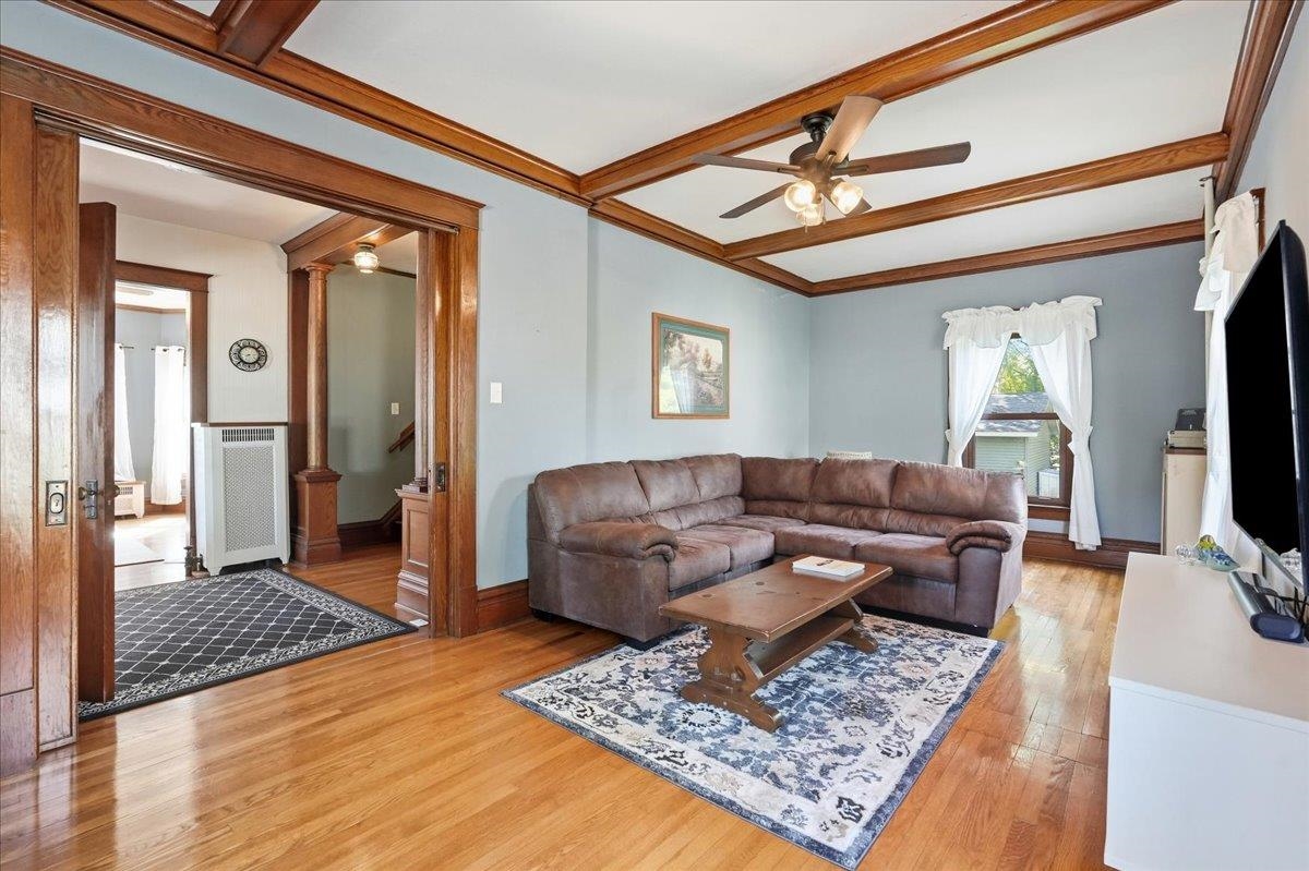 Living room with a brown sectional, patterned rug, and prominent dark wood ceiling beams.