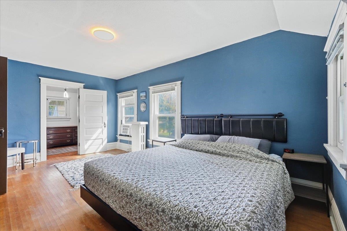 Bedroom with blue walls, a large patterned bed, hardwood floors, and an open doorway to an adjoining room.