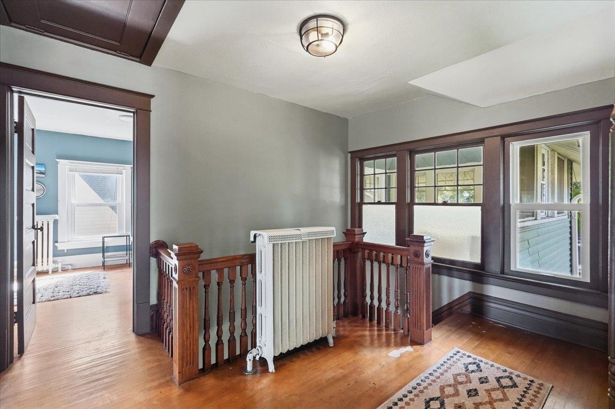 Upper landing with dark wood railings, hardwood floors, a radiator, and tall frosted windows.