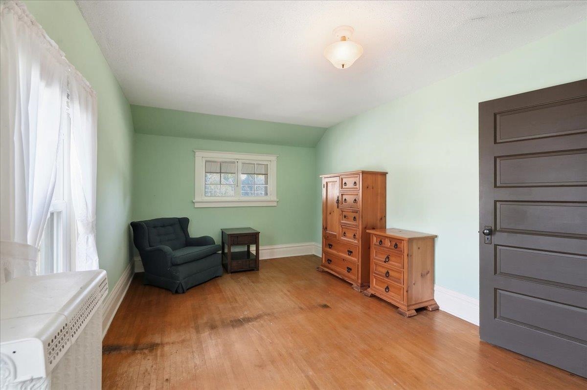 Room with mint-green walls, hardwood floors, a dark armchair, and wooden dressers.
