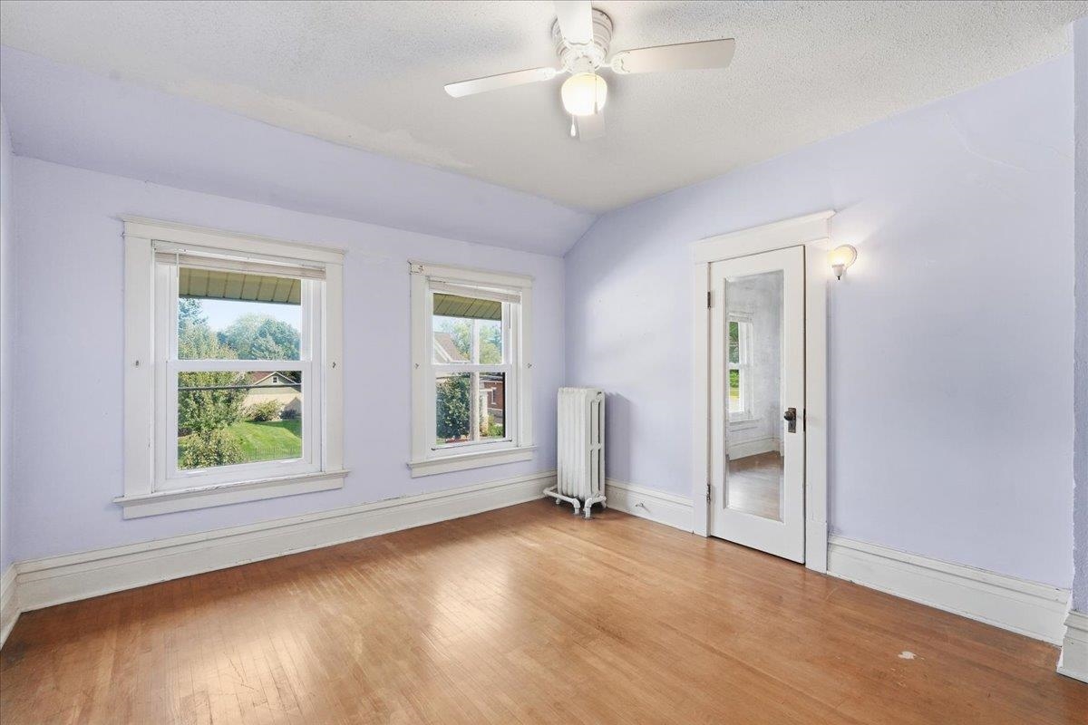 Empty room with hardwood floors, two windows, a radiator, and a glass-panel door.
