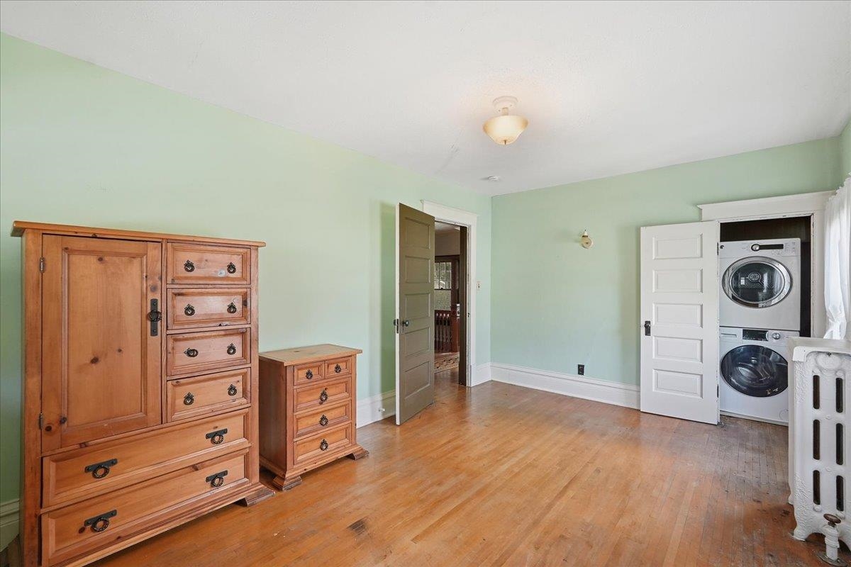 Bedroom with hardwood floors, wooden dressers, a stacked washer and dryer, and part of a white crib.