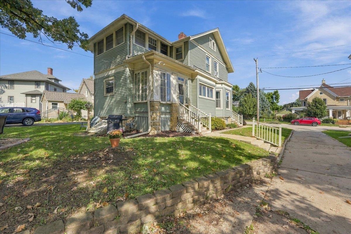 Two-story sage-green house with a stone-accented porch and low front retaining wall.